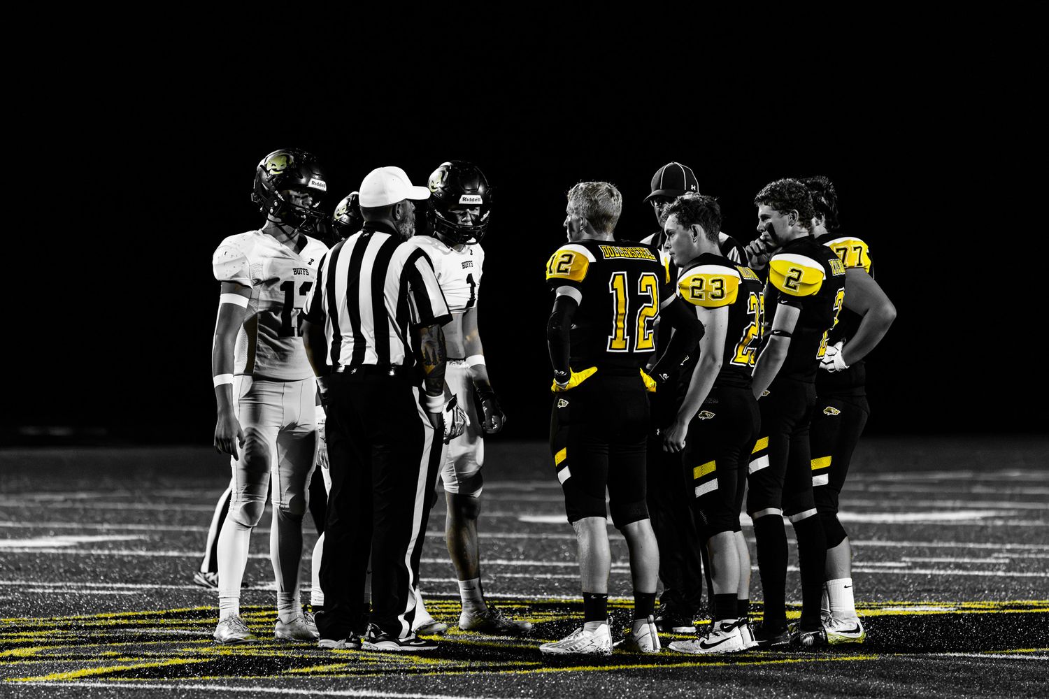 Football players and referee gather for a coin toss before a nighttime high school football game.