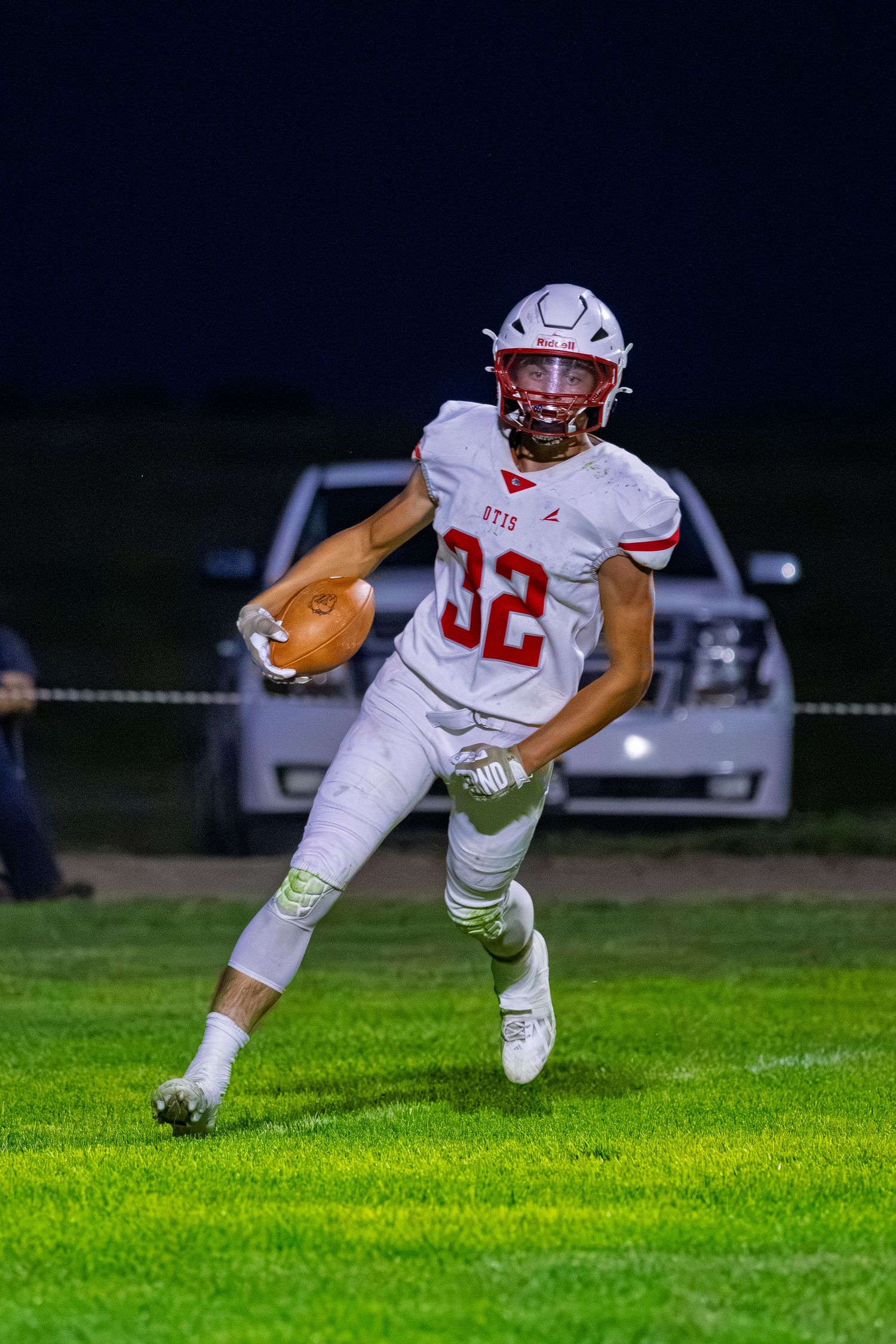 High school football player number 32 in white uniform running with the ball during a night game.