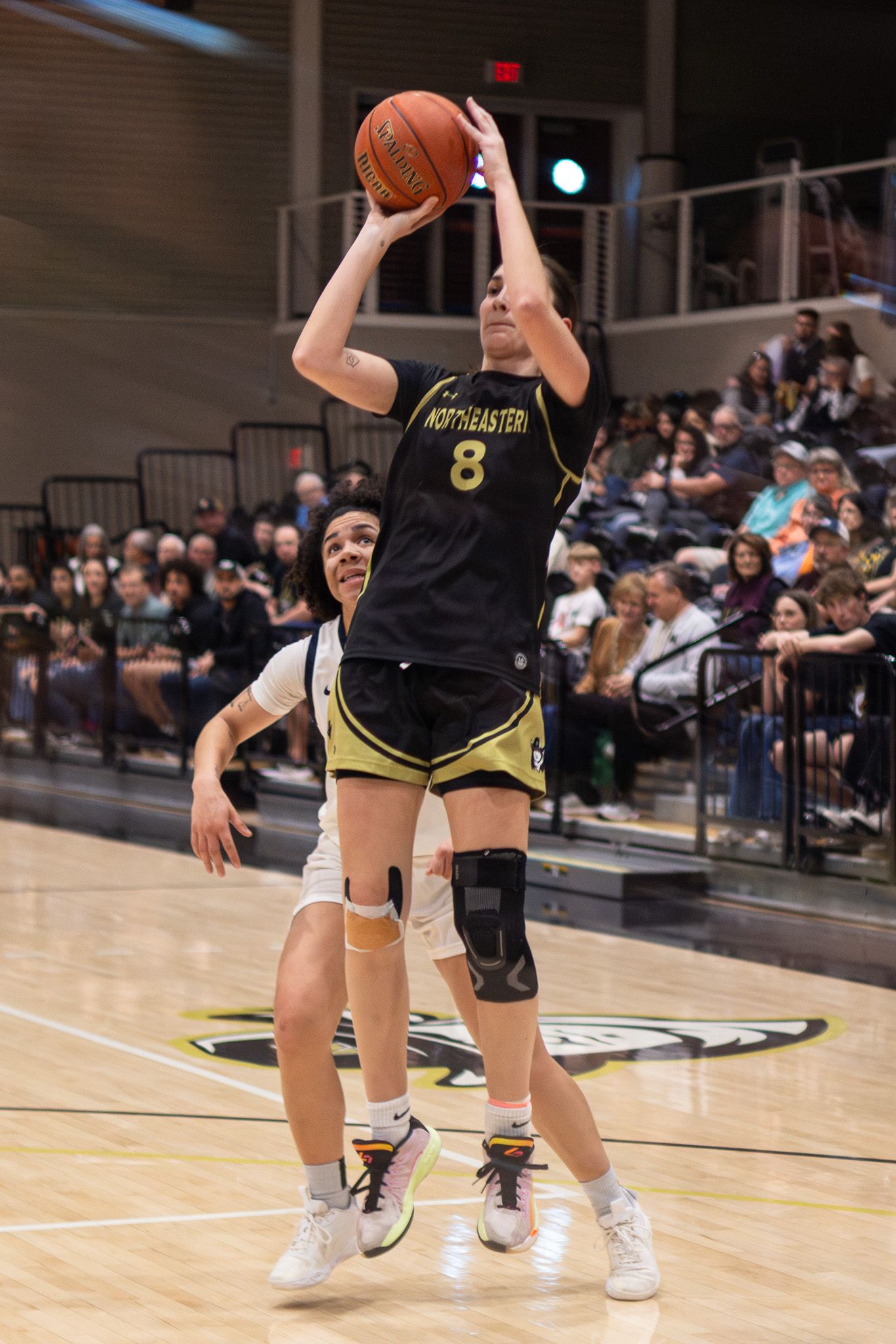 Female basketball player number 8 in black Northeastern uniform rises for a jump shot during a game.