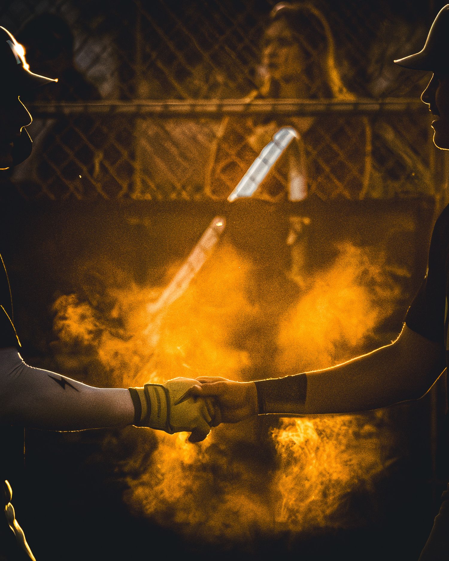 Two baseball players fist bump in front of a dramatic golden cloud of dust during a game.