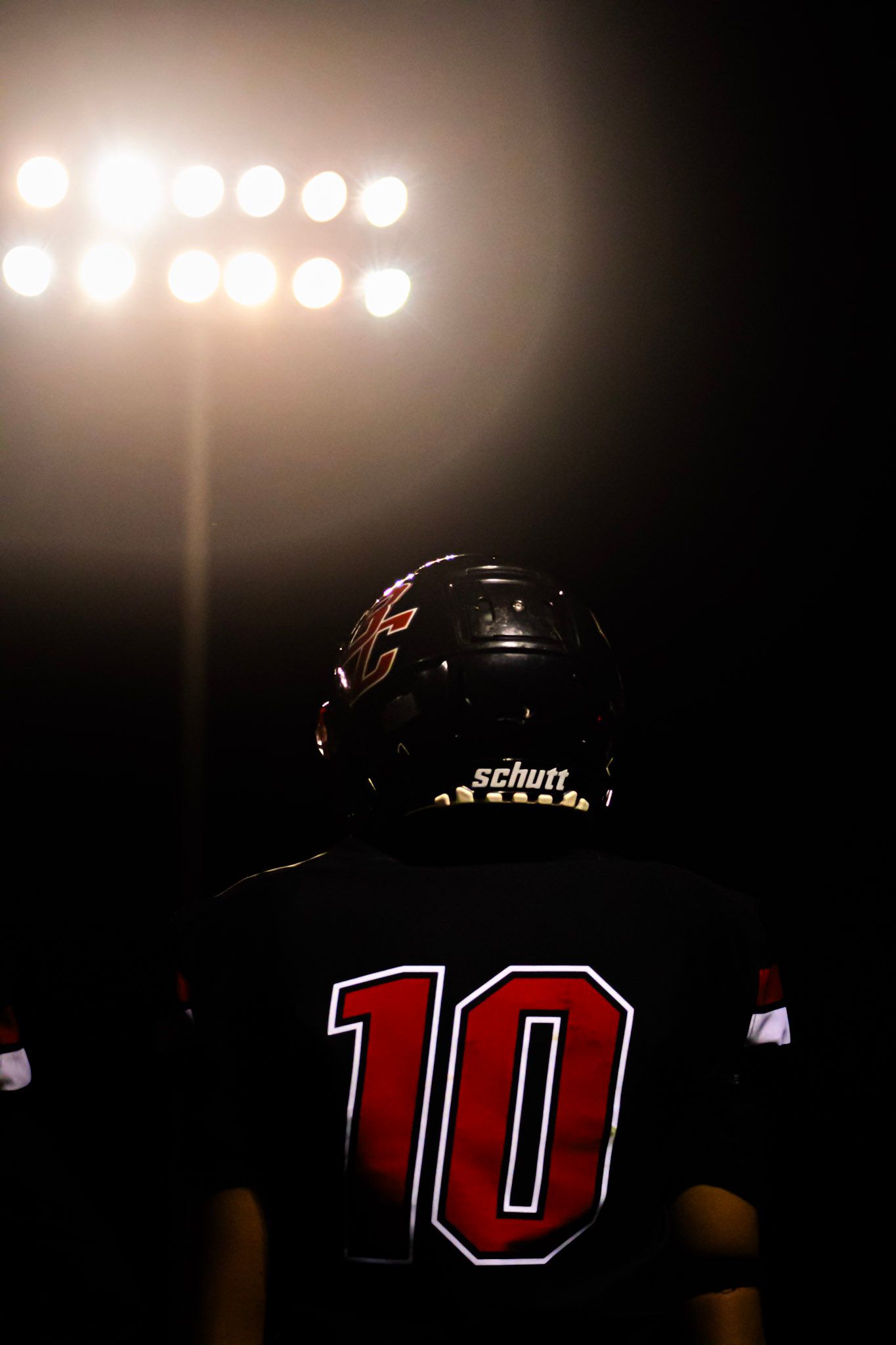 Football player wearing number 10 jersey and Schutt helmet standing under stadium lights at night.