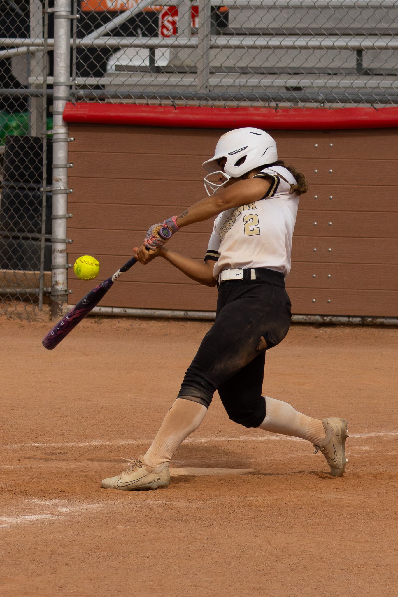 Young softball player wearing number 2 makes contact with yellow ball during at-bat.