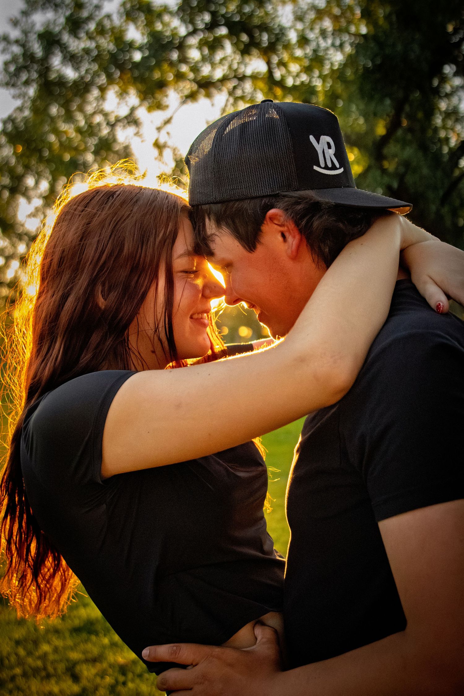 Couple sharing a tender moment at golden hour with warm sunlight glowing behind them.