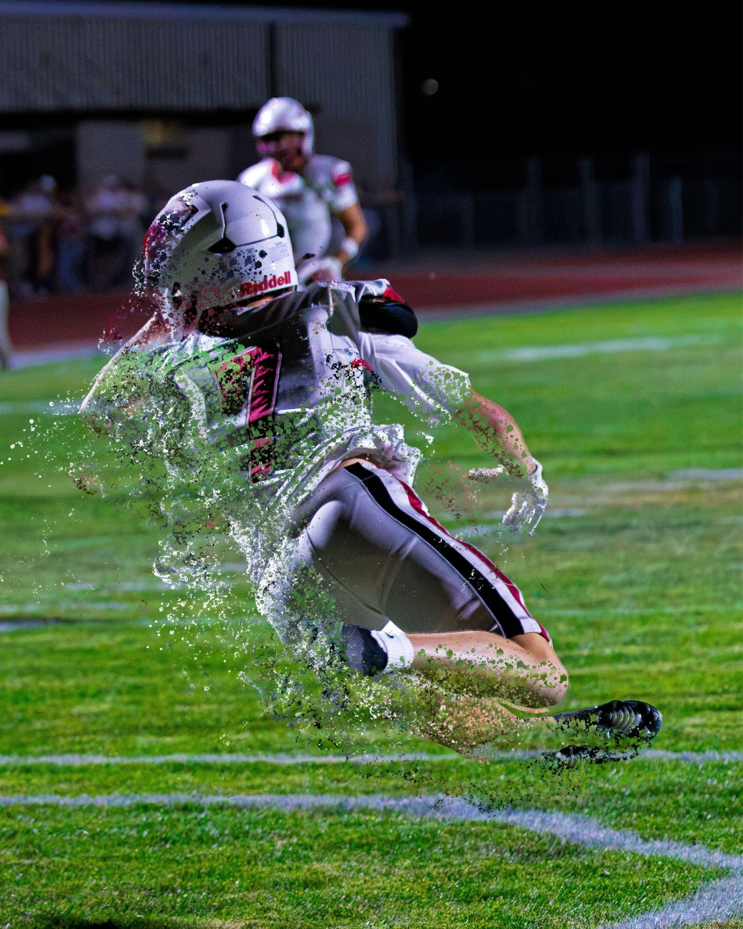 Football player sliding on wet grass field at night game with dramatic water splash effect.