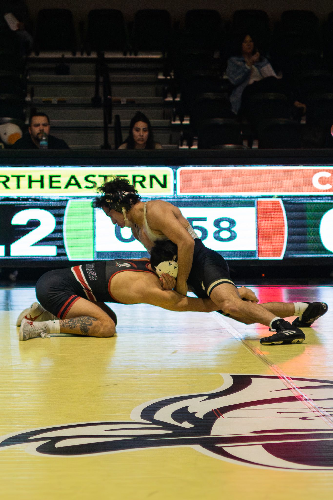 Two wrestlers compete intensely on the mat during a college wrestling match at Northeastern University.