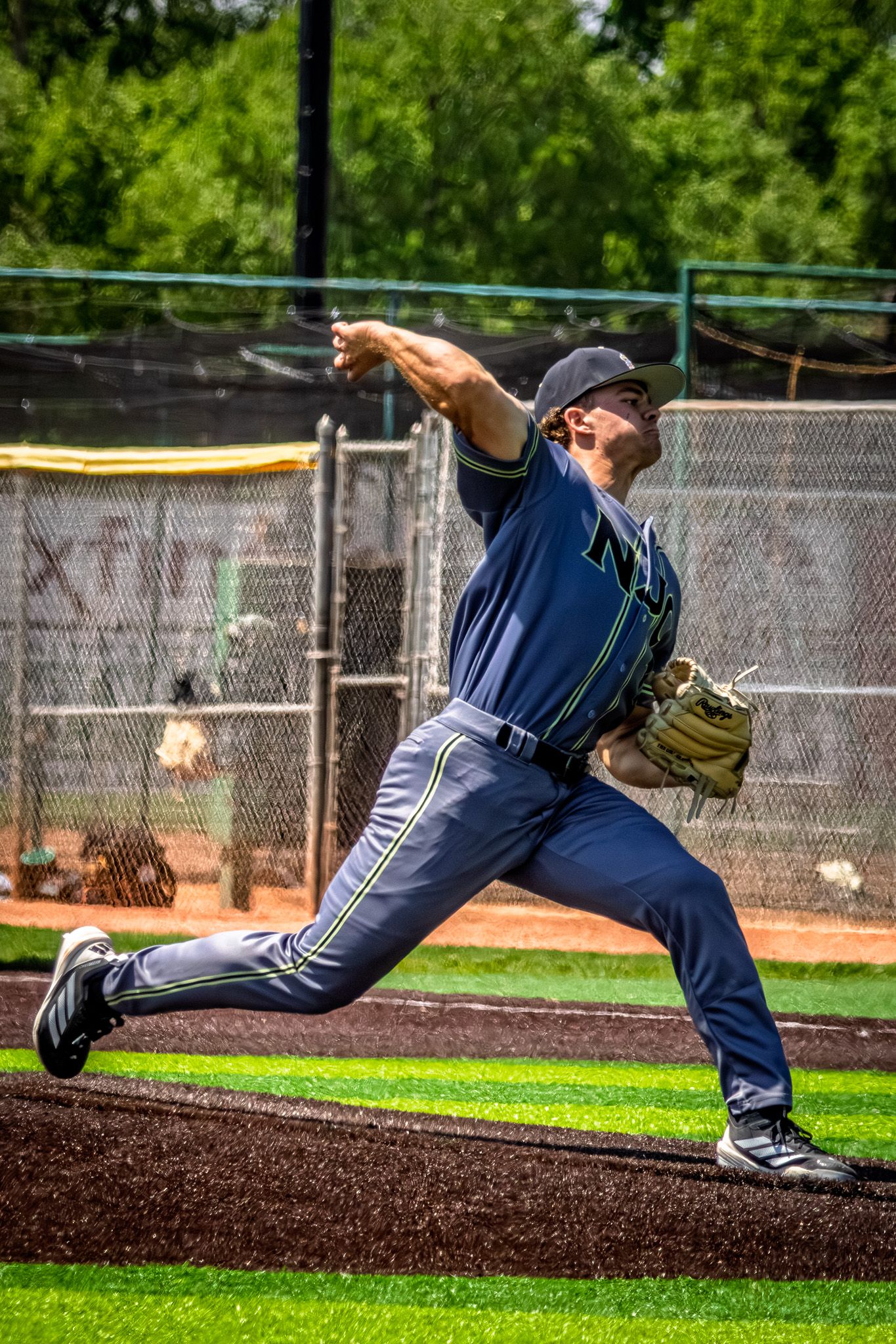 A baseball pitcher in navy uniform delivers a powerful throw during an outdoor game on a sunny day.