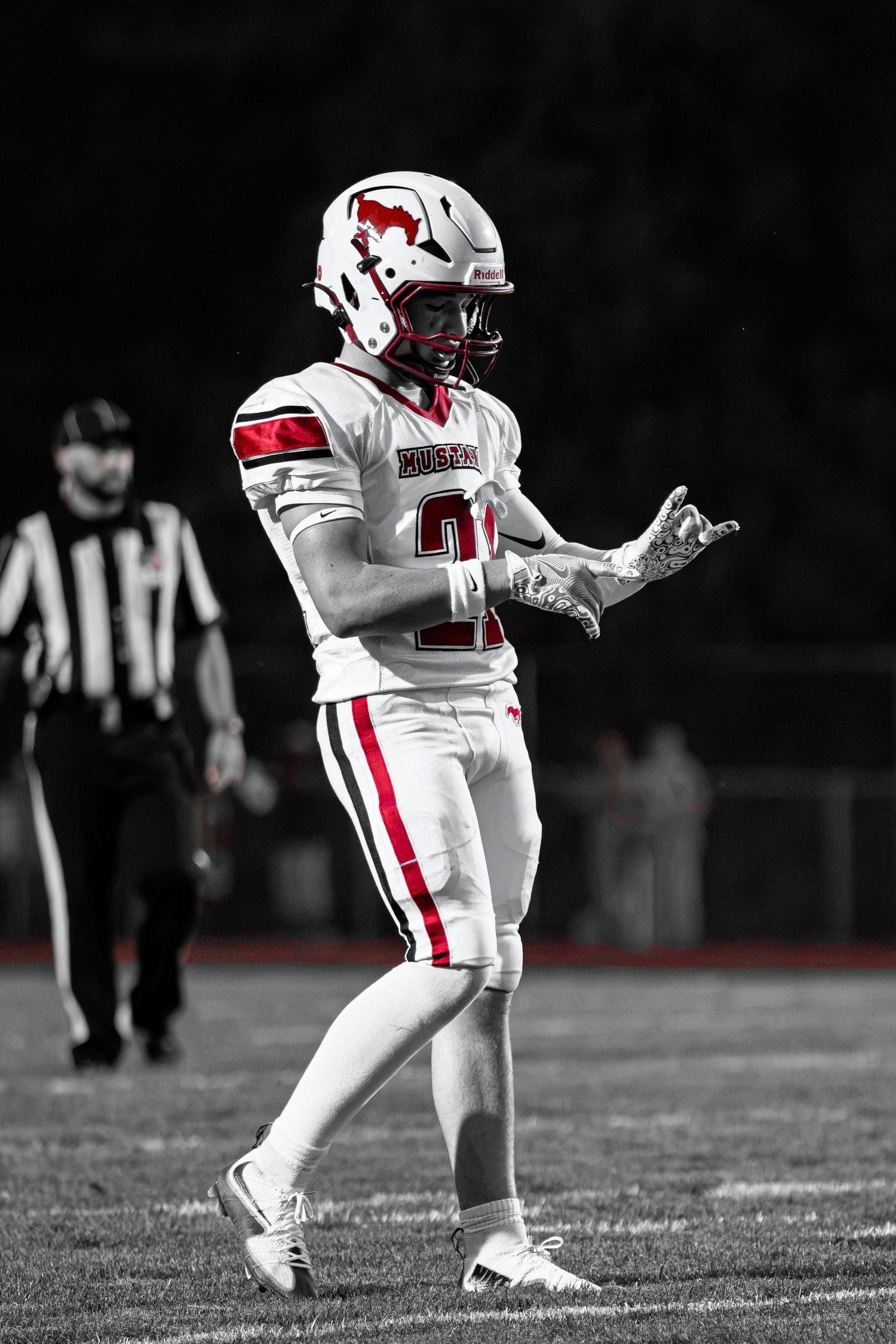 Selective color photo of football player #21 in red and white uniform gesturing on field with referee behind.
