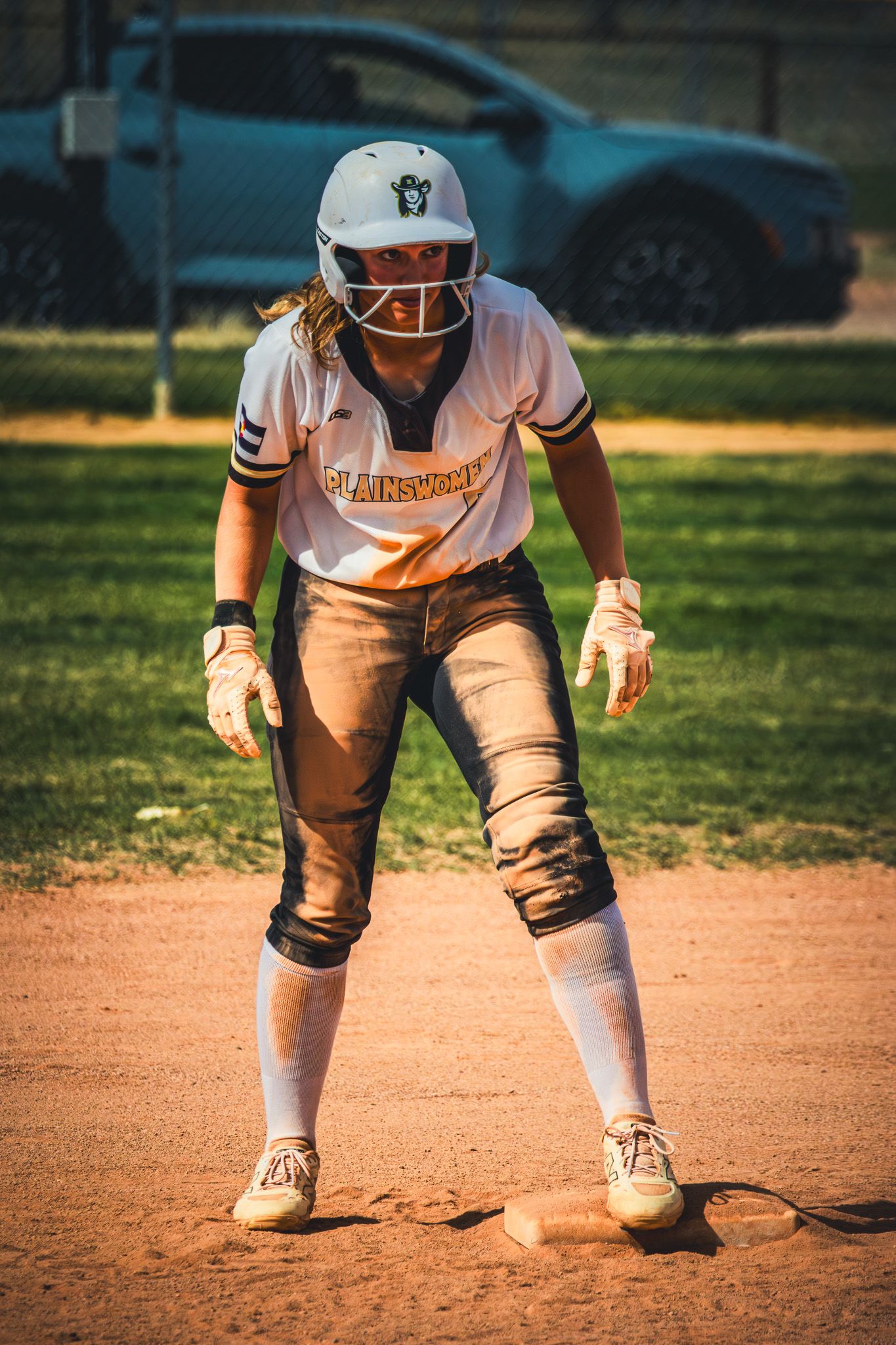 Softball player in Plainsmen uniform crouches in ready position on base during a game.