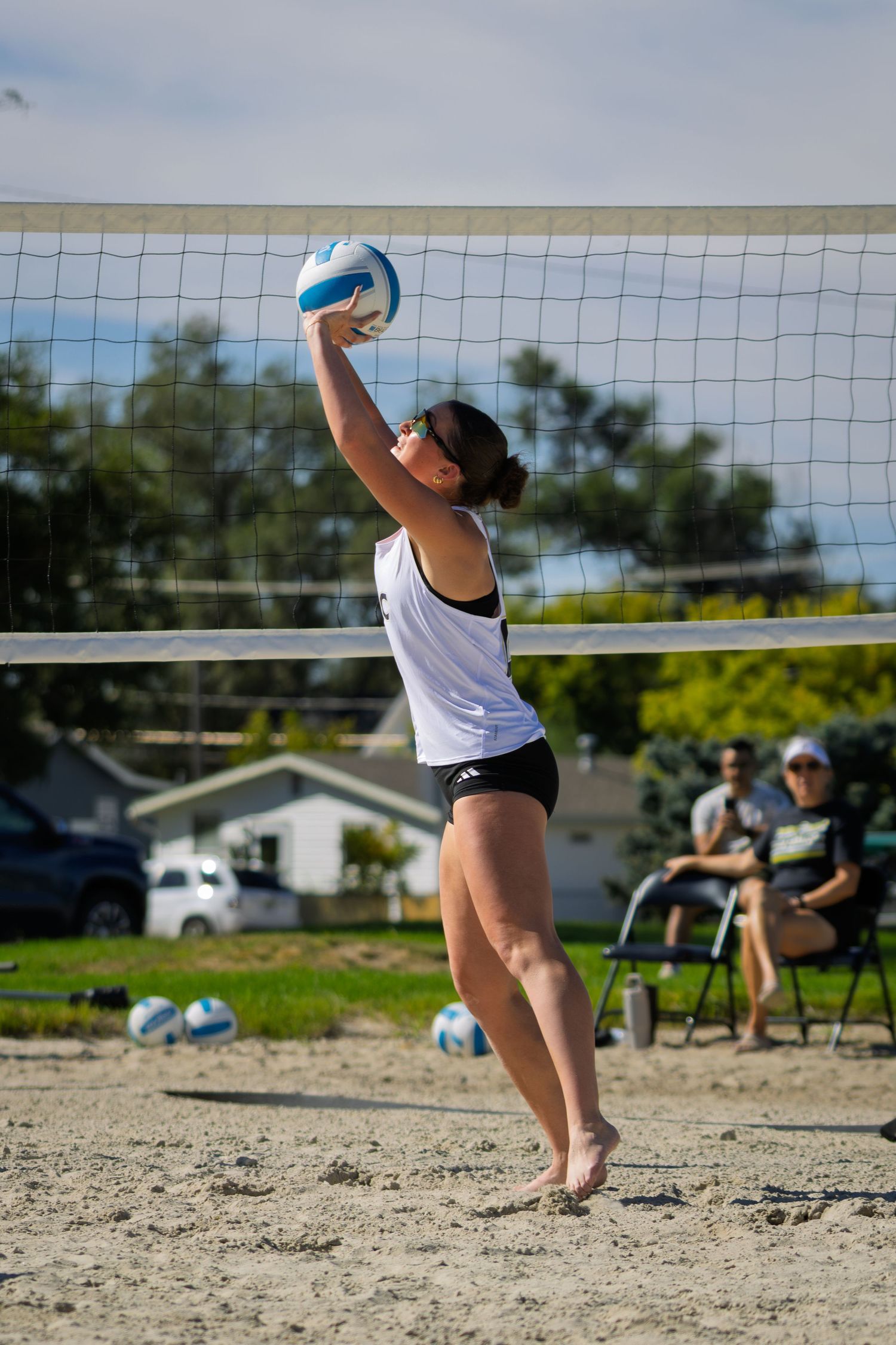 Female beach volleyball player in white top setting the ball at the net during an outdoor sand volleyball match.
