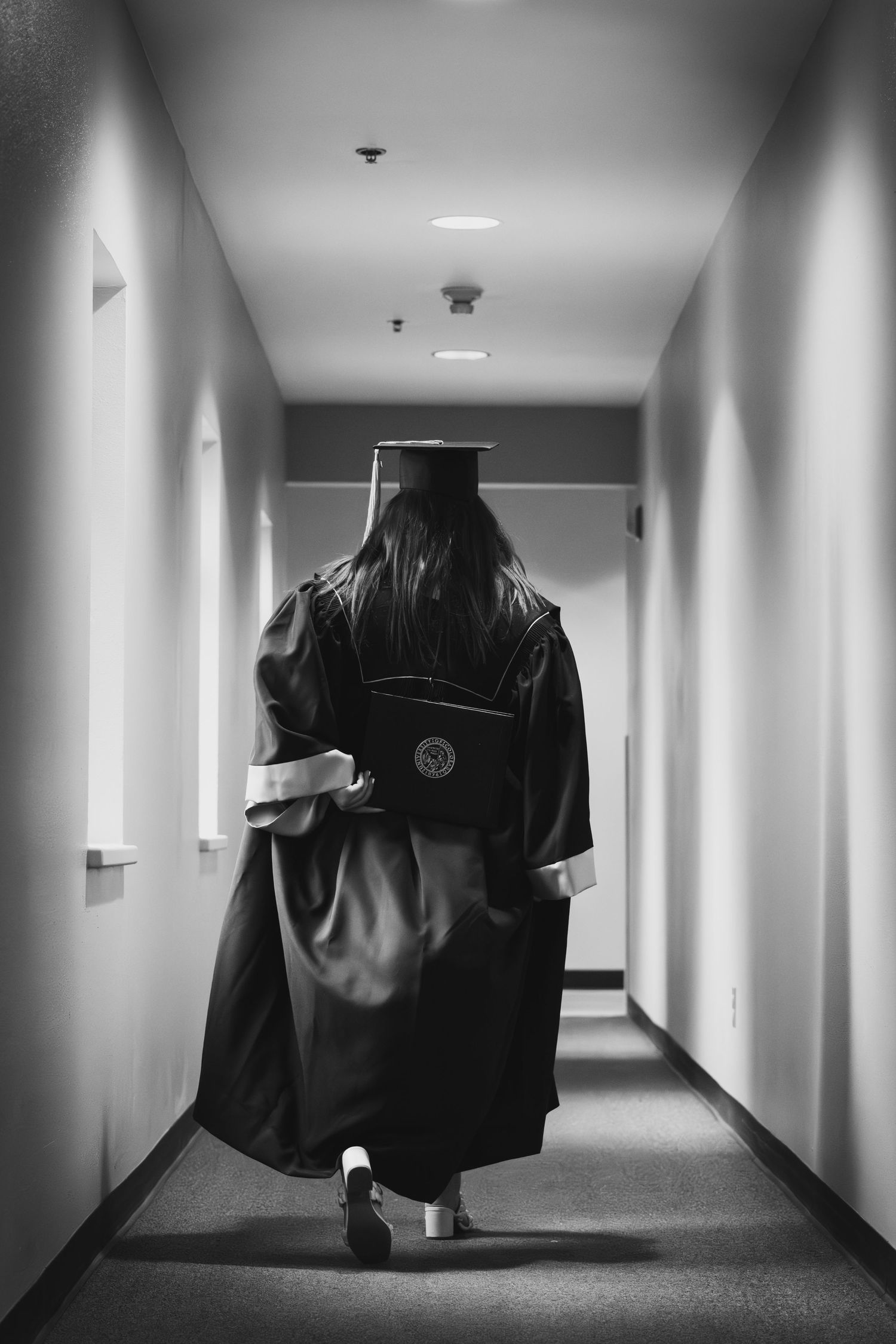 Black and white photo of graduate in cap and gown walking down a hallway.