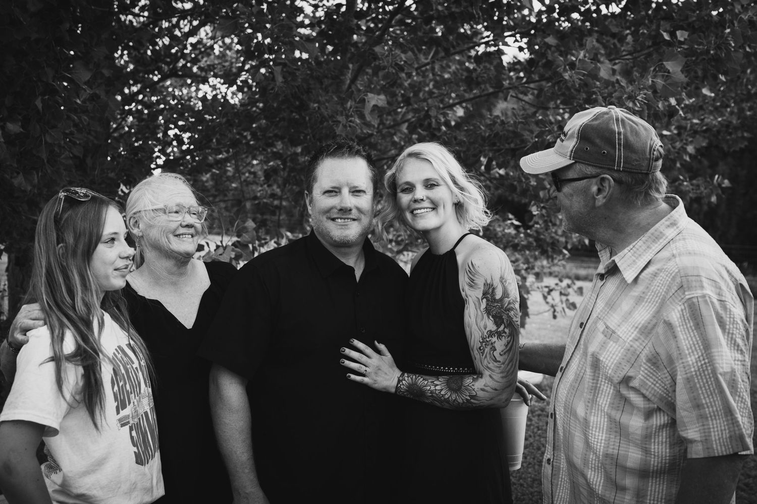 Black and white photo of five smiling family members gathered together outdoors under trees.