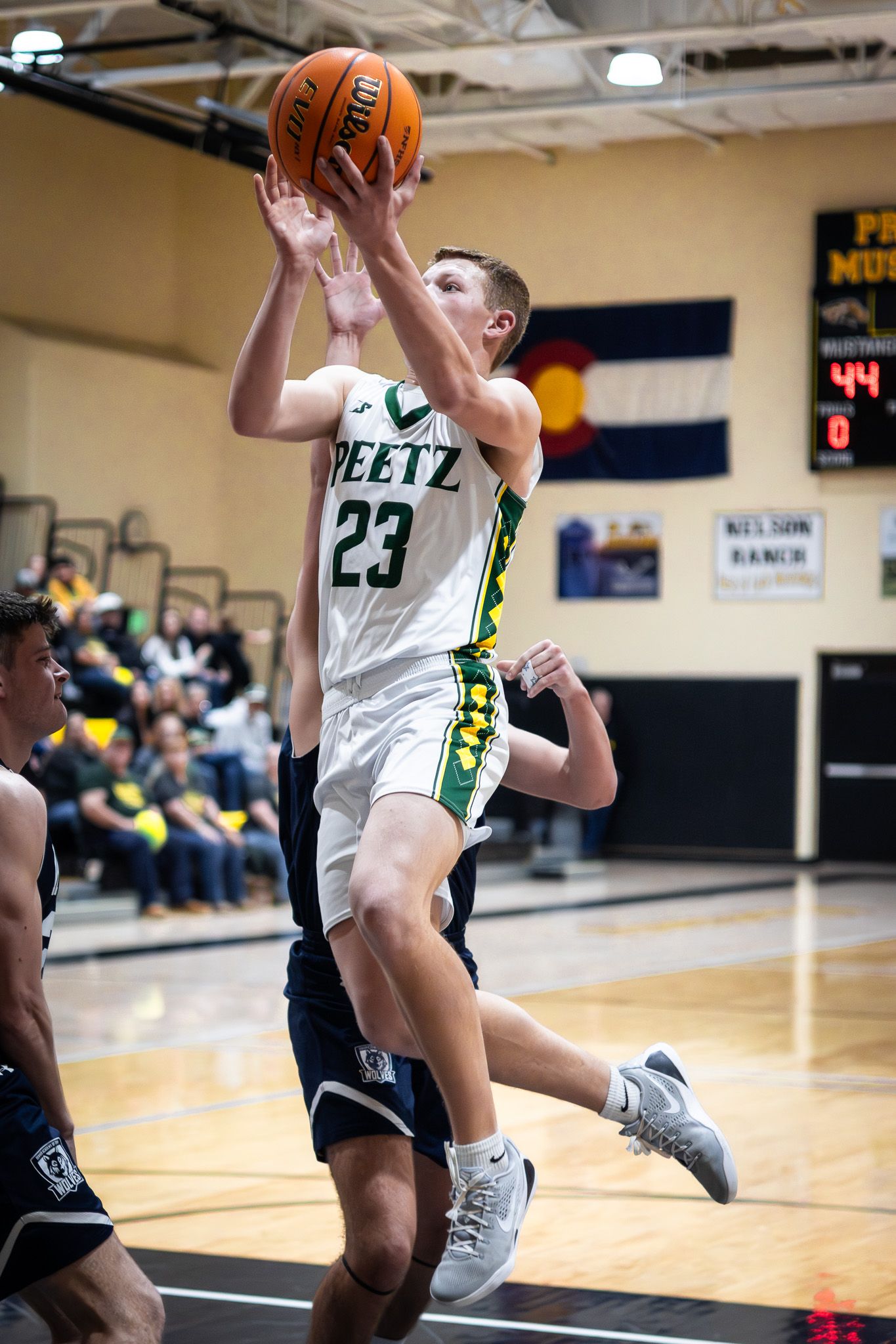 A Peetz High School basketball player number 23 leaps for a layup shot during an indoor game.