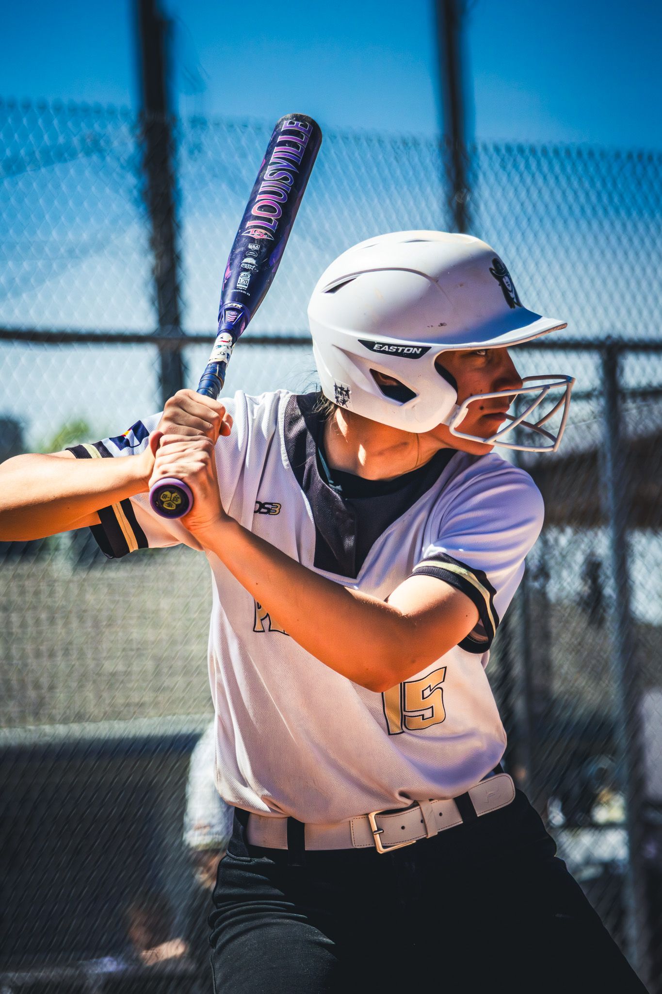 Young softball batter in white jersey number 15 ready to swing with Easton helmet.