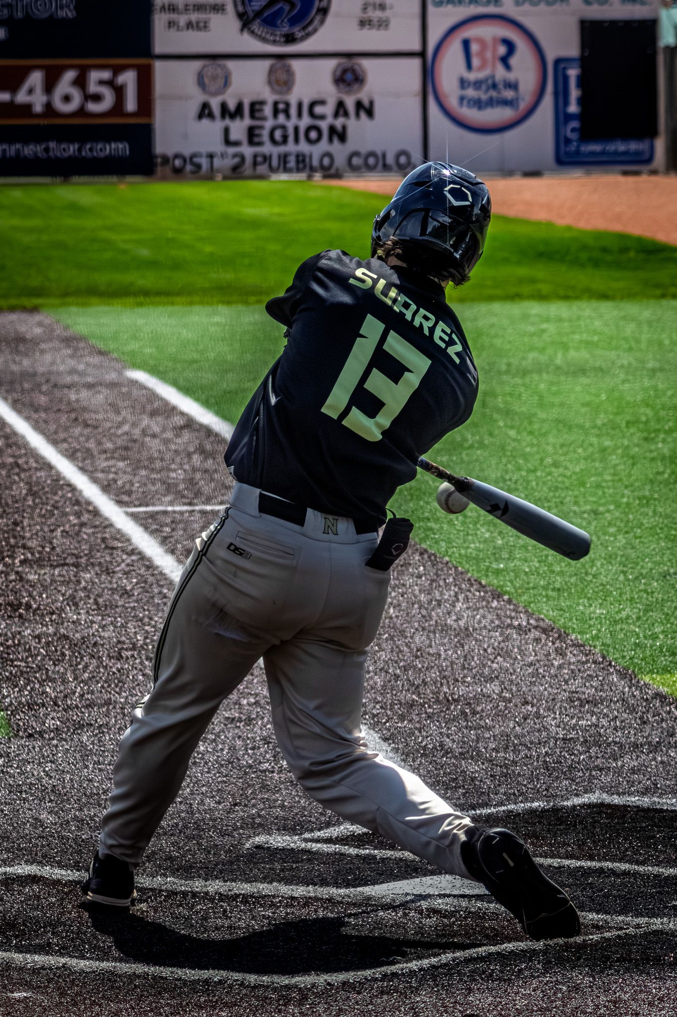 Baseball batter Suarez number 13 swings at a pitch during a game at an American Legion baseball field.