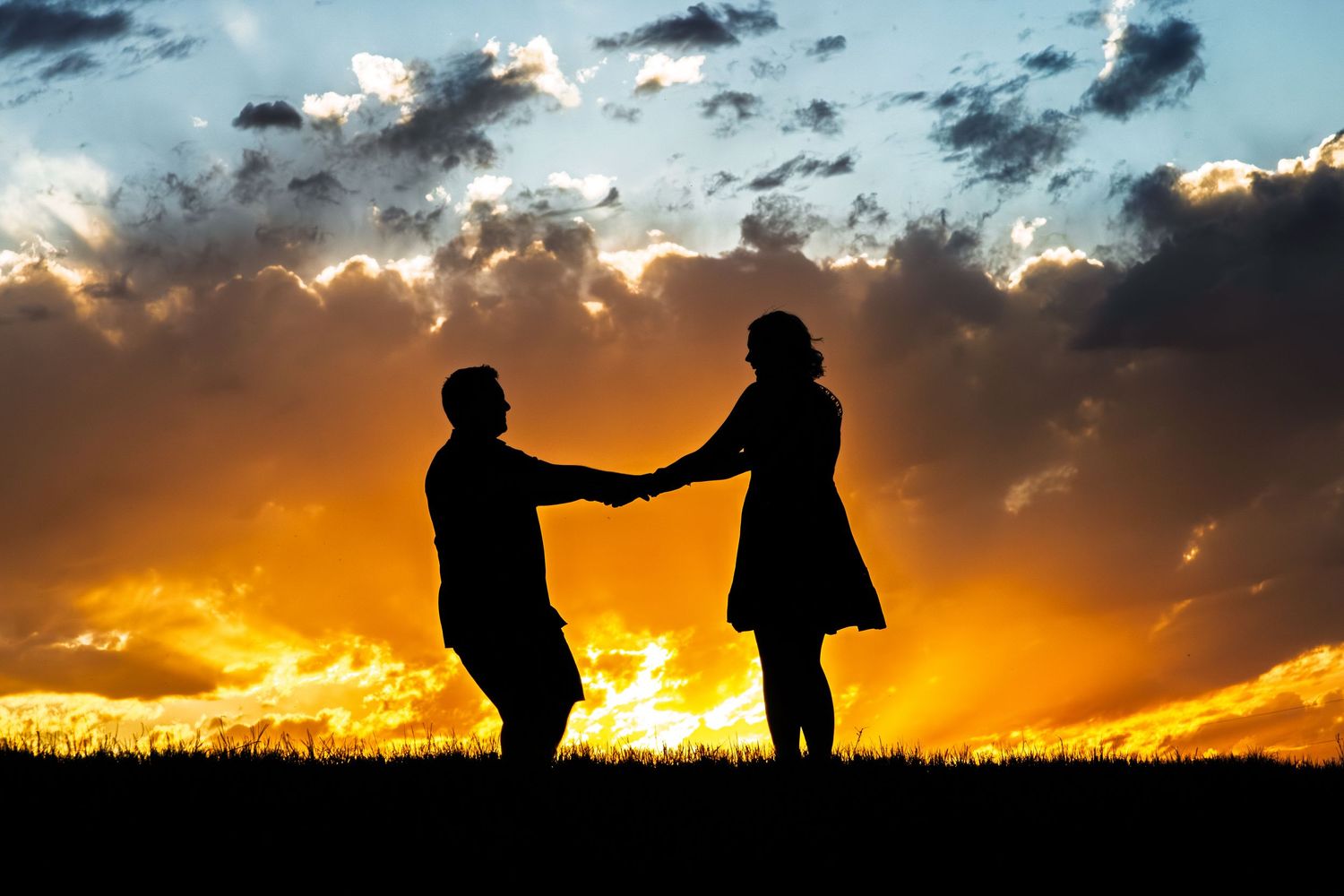 Romantic couple silhouette holding hands against a dramatic golden sunset sky.