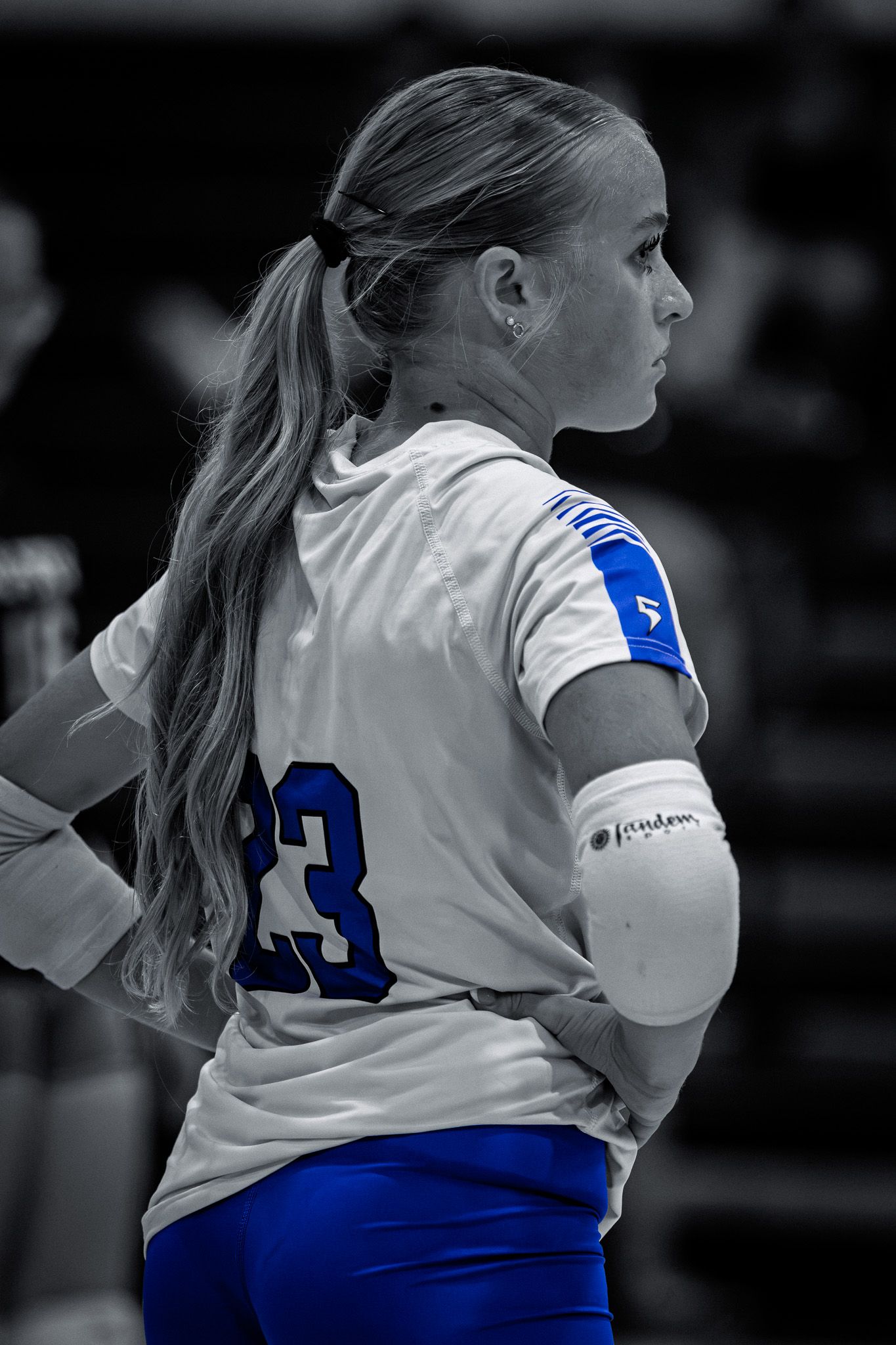 Female volleyball player #23 in white and blue uniform with elbow pad, selective color photography.