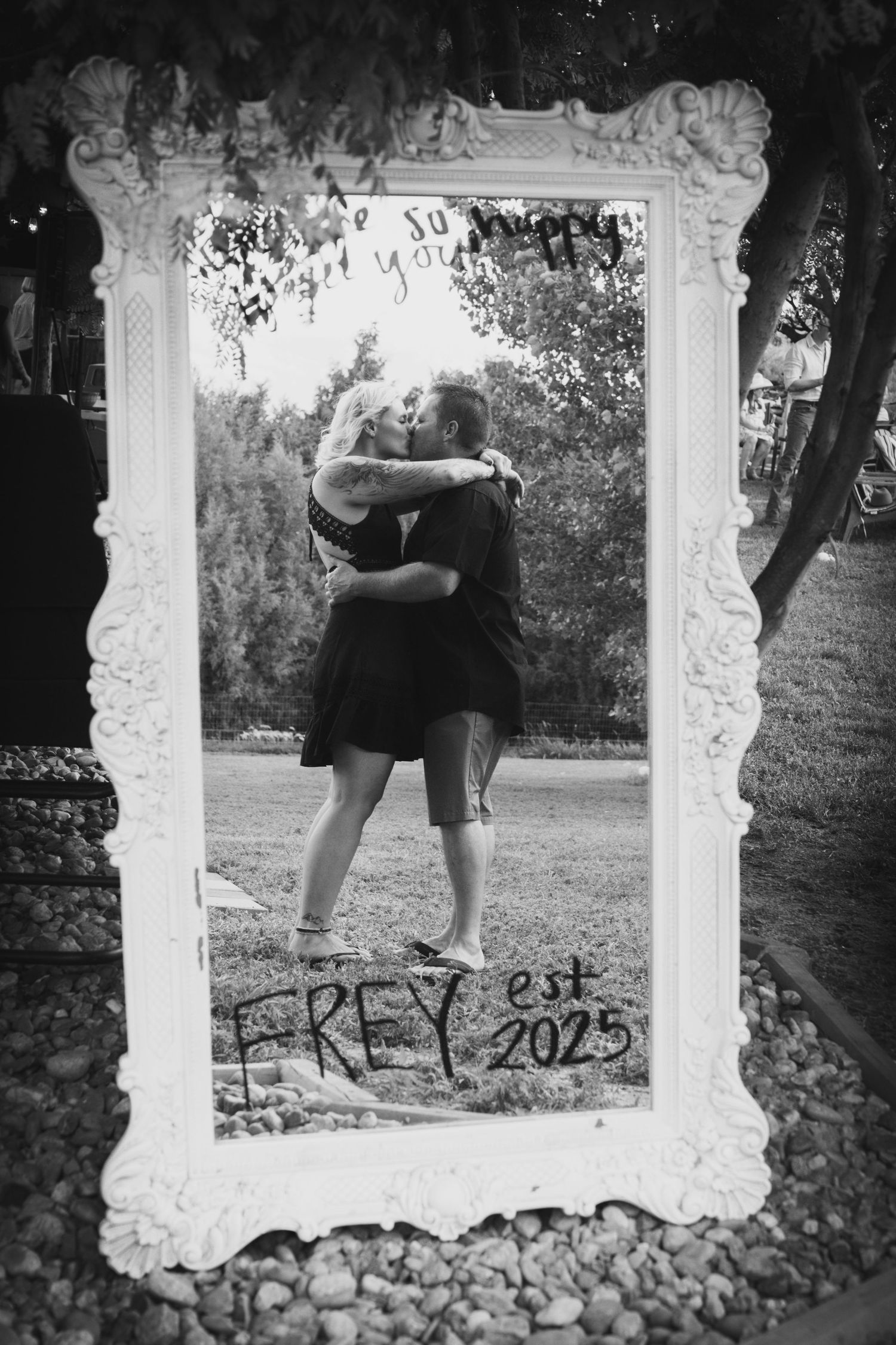 Black and white photo of couple kissing in decorative white mirror frame, Frey est 2025.