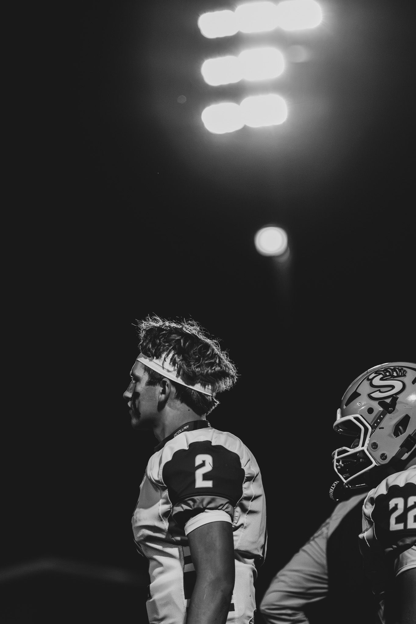 Black and white photo of football player number 2 standing under stadium lights during night game.