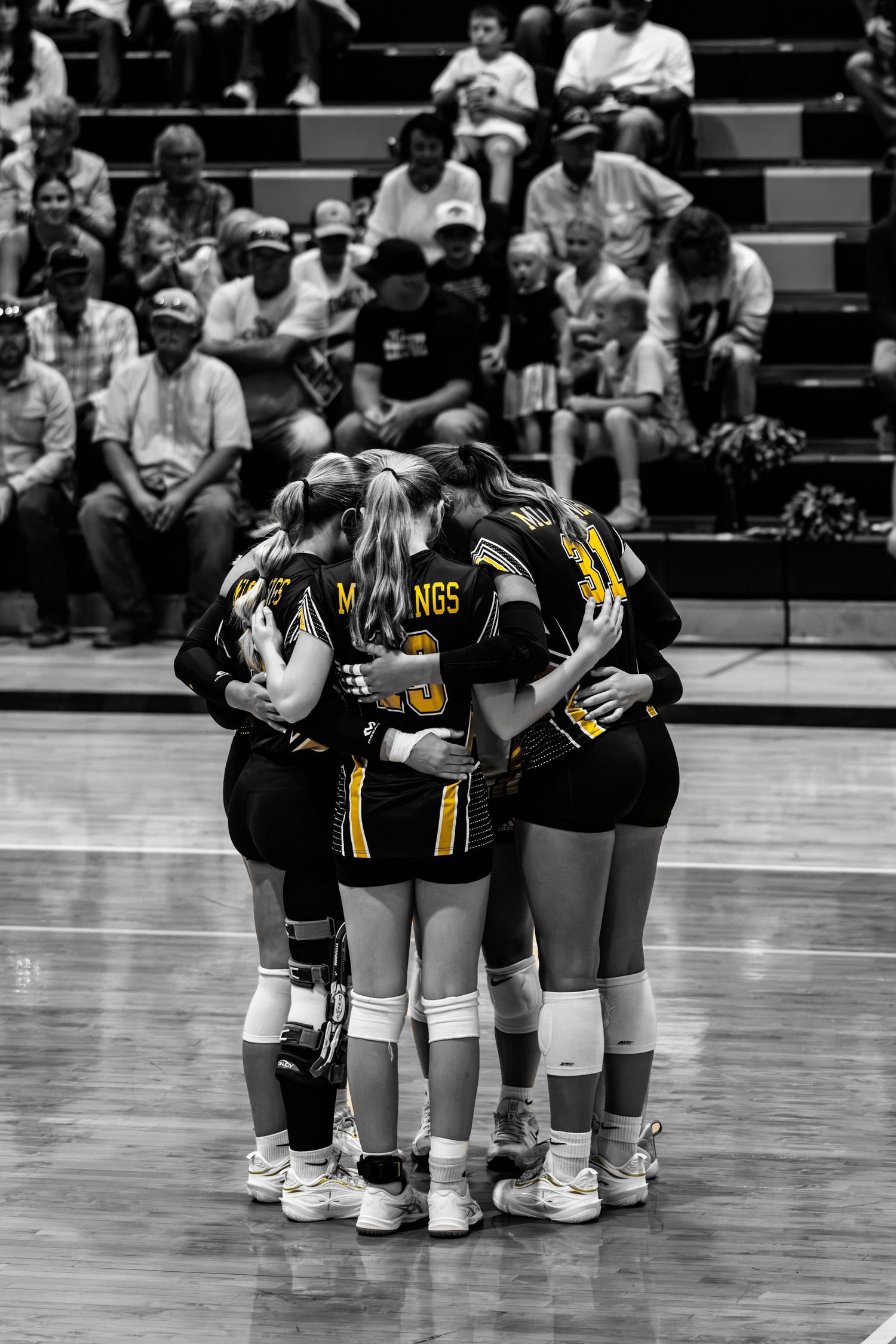 Black and white photo of Mustangs volleyball team huddling together on the court during a match.