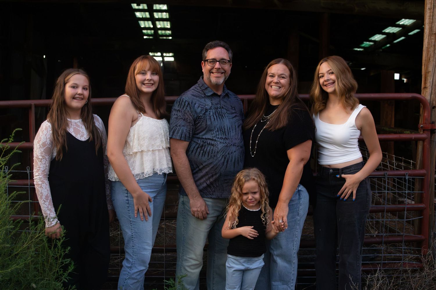 Happy family of six smiles together outside a rustic barn in casual denim outfits.