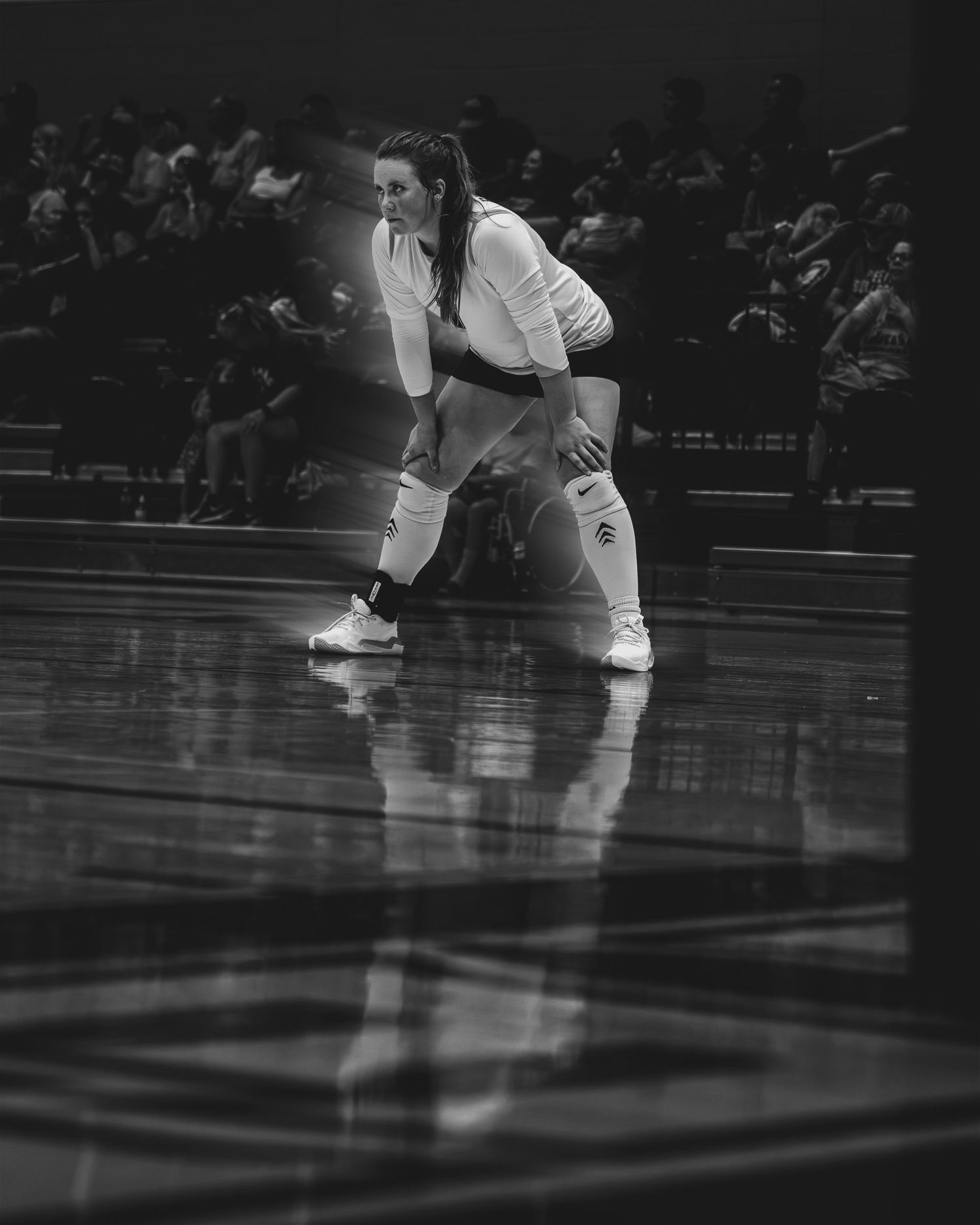 Female volleyball player in white uniform crouches in defensive ready position on reflective court.