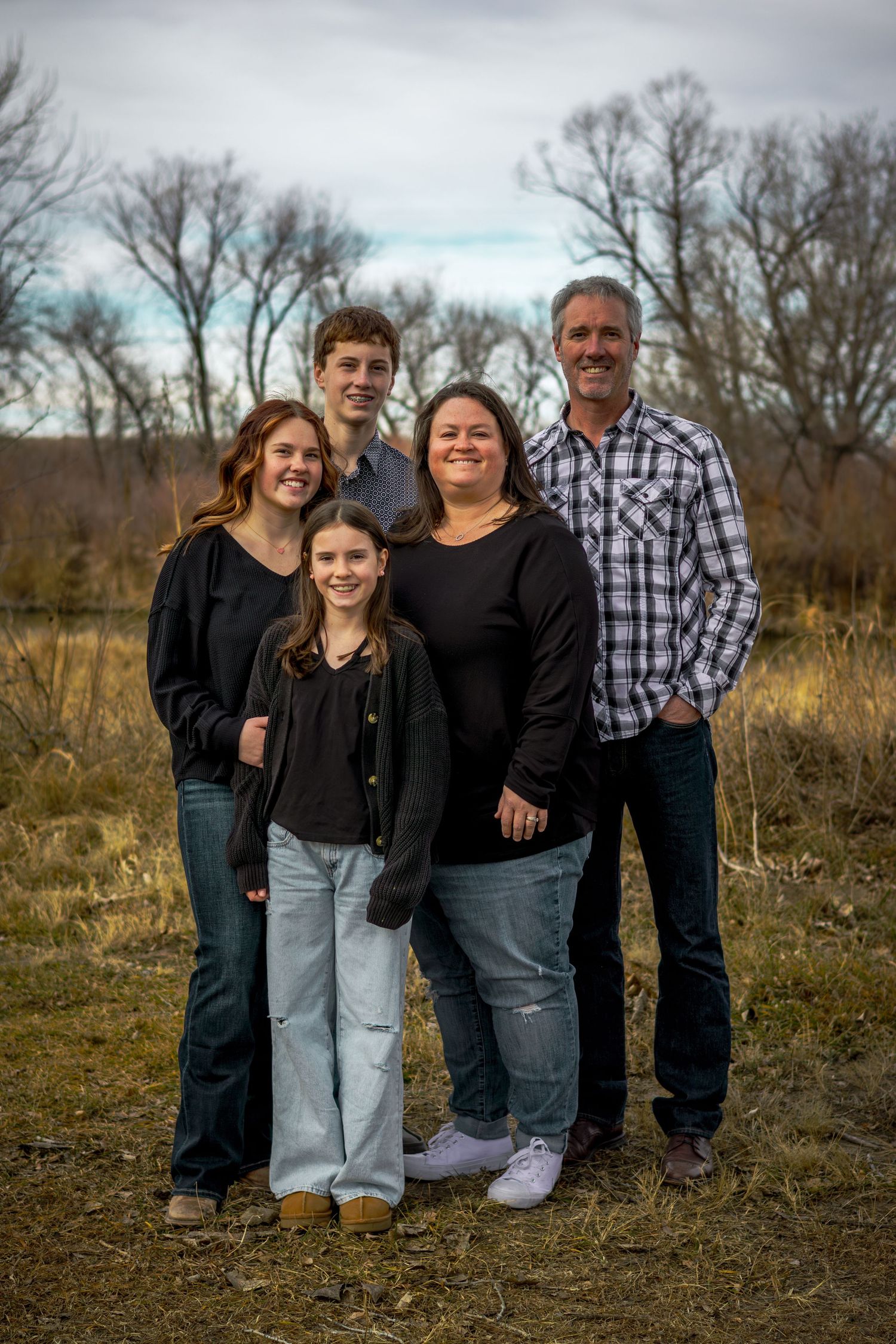 Family of five posing together in a field with bare trees during autumn.