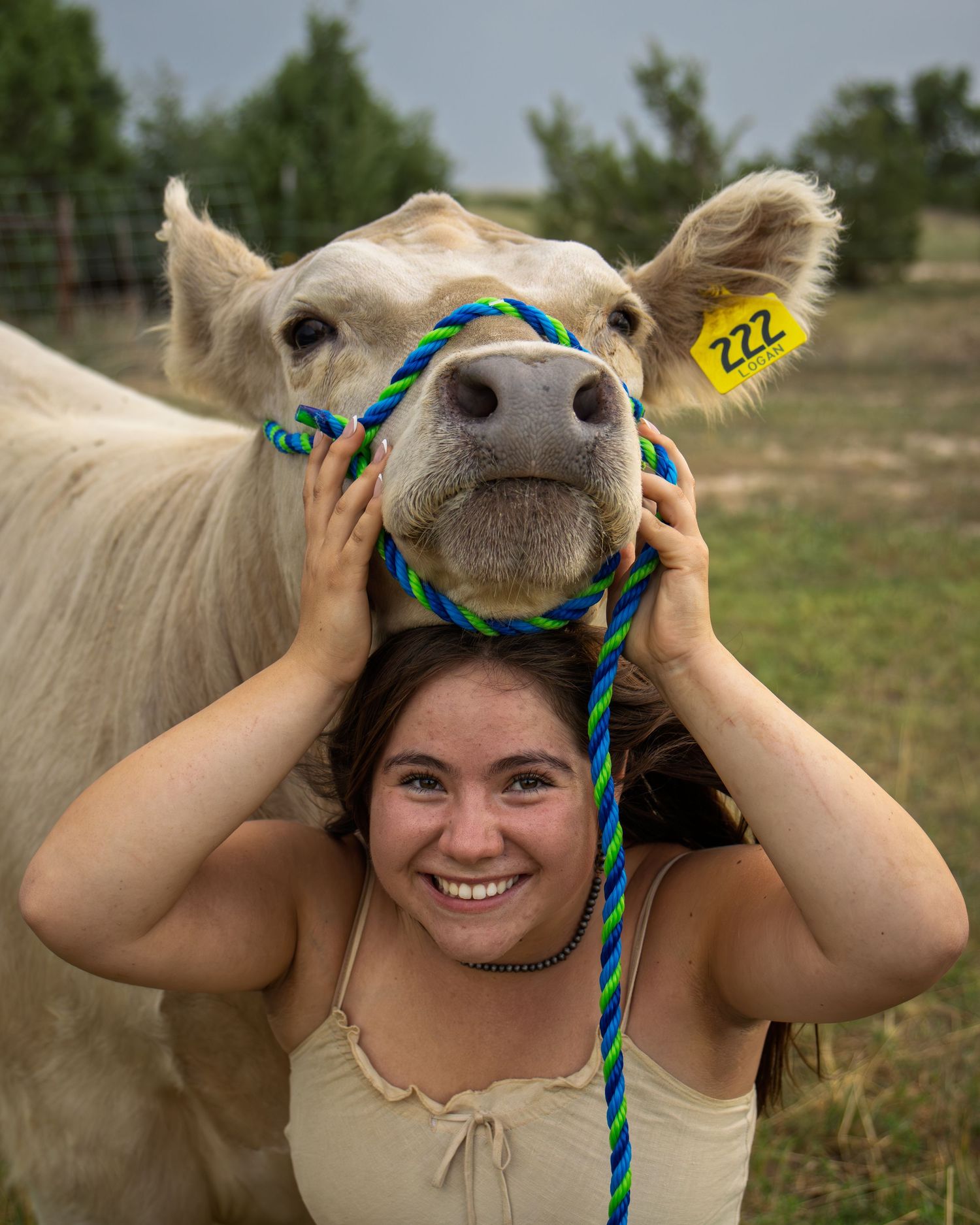 Smiling young woman poses with cream colored show cow numbered 222 resting chin on her head.