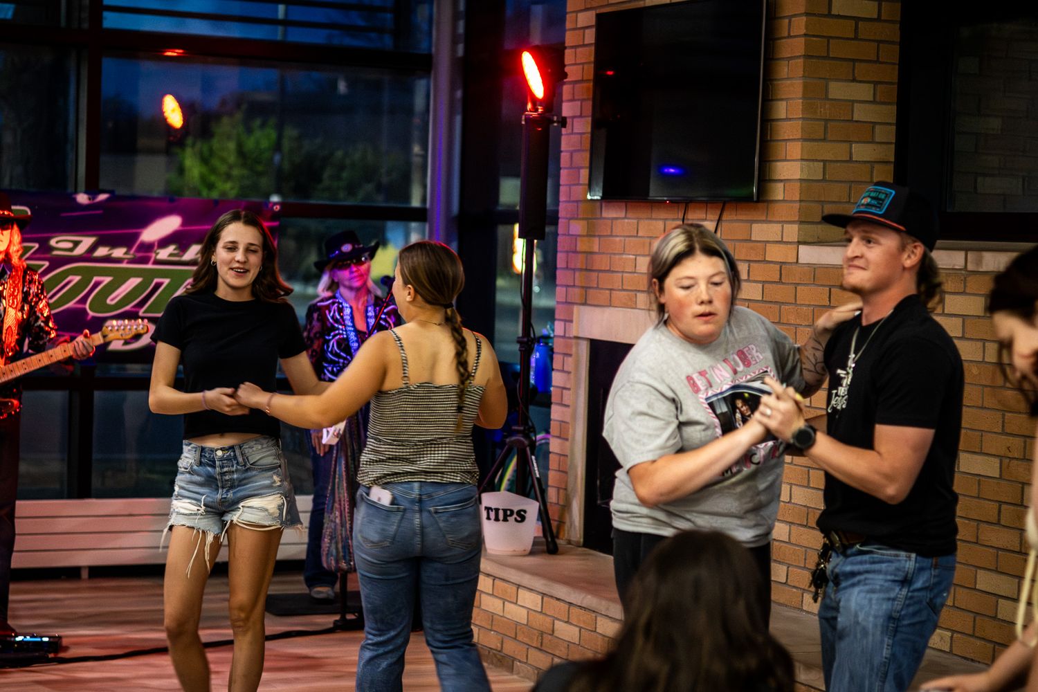 Group of people dancing and socializing at an outdoor evening event with string lights and brick walls.