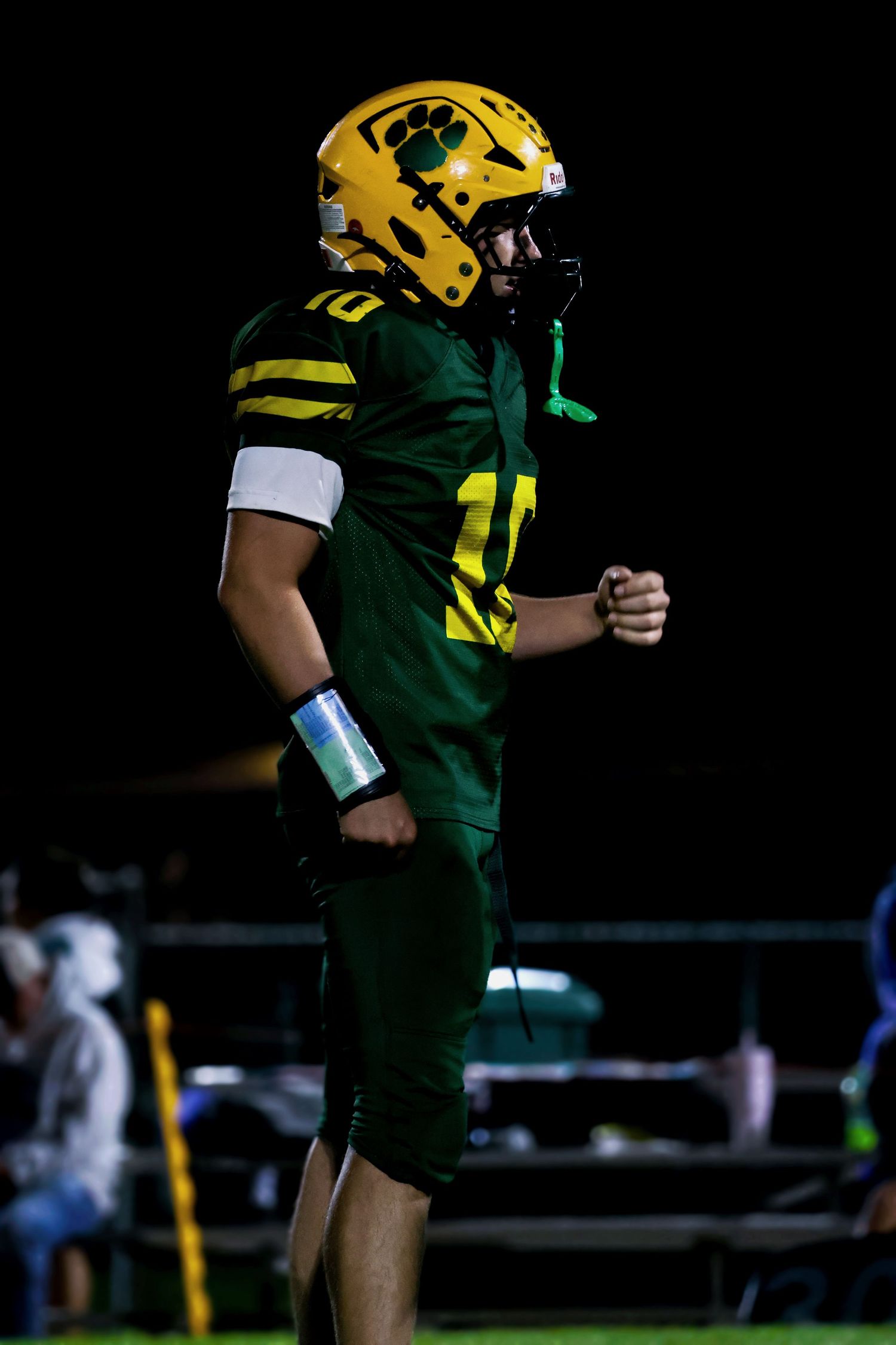 Football player wearing green and gold uniform #10 standing on field during night game.