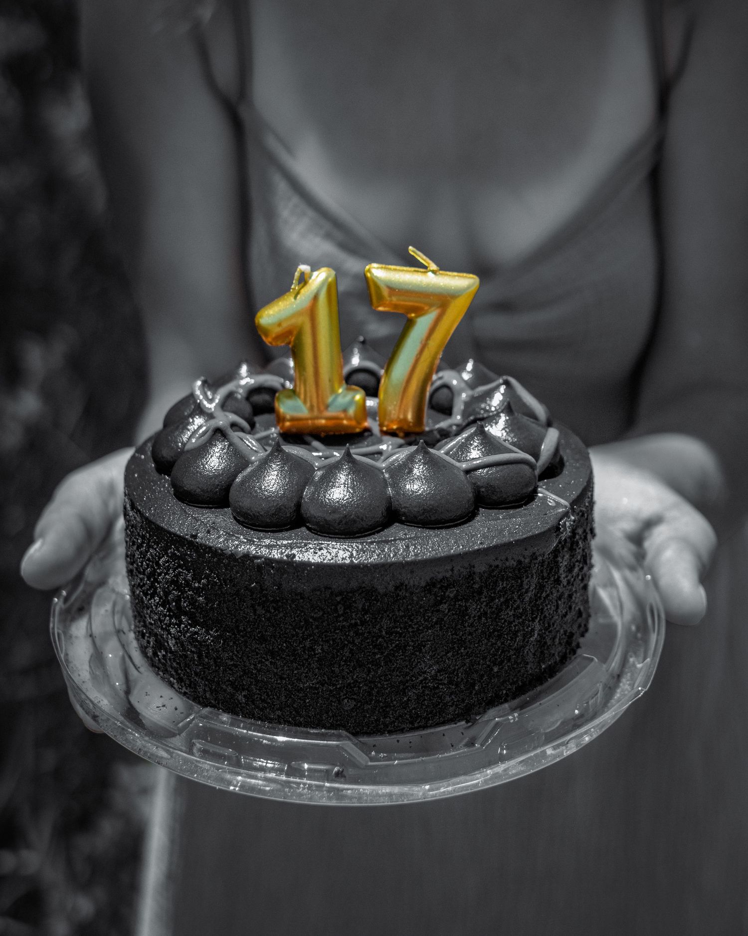 Person holding a dark chocolate birthday cake with gold number 17 candles.