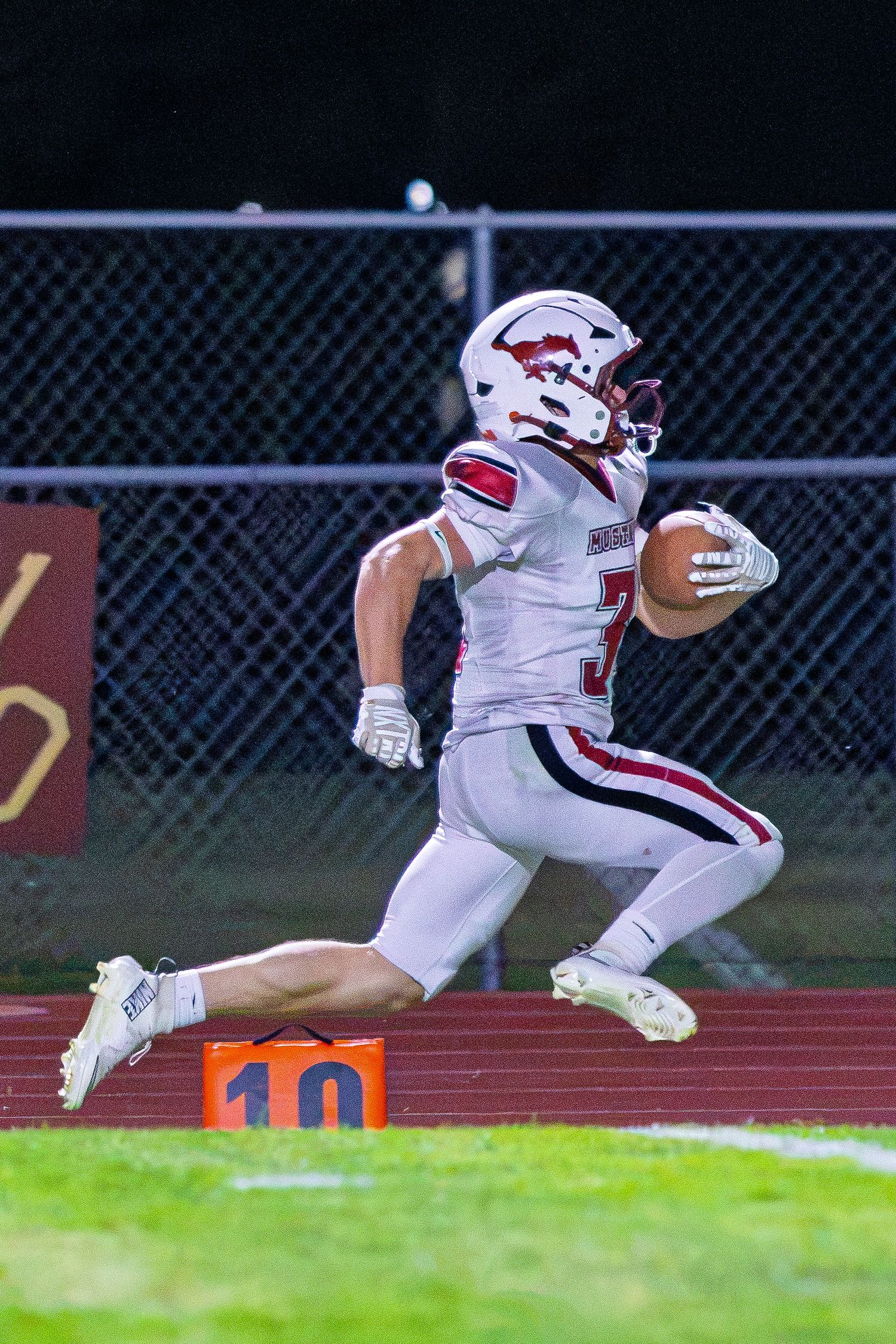 Football player #3 in white and red uniform sprints along the sideline during a night game.