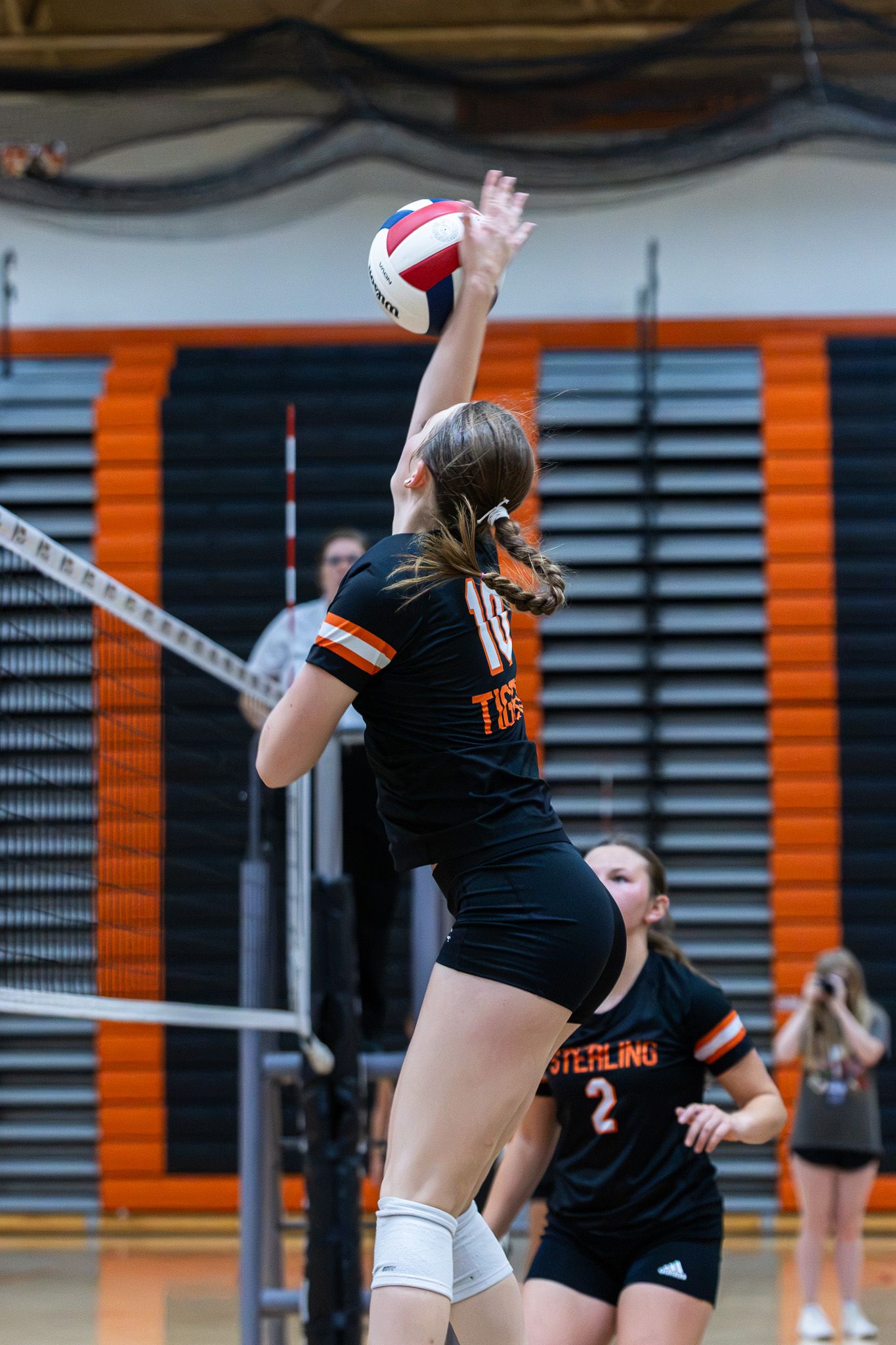 Tigers volleyball player #10 leaps to spike the ball as teammate #2 watches from behind.