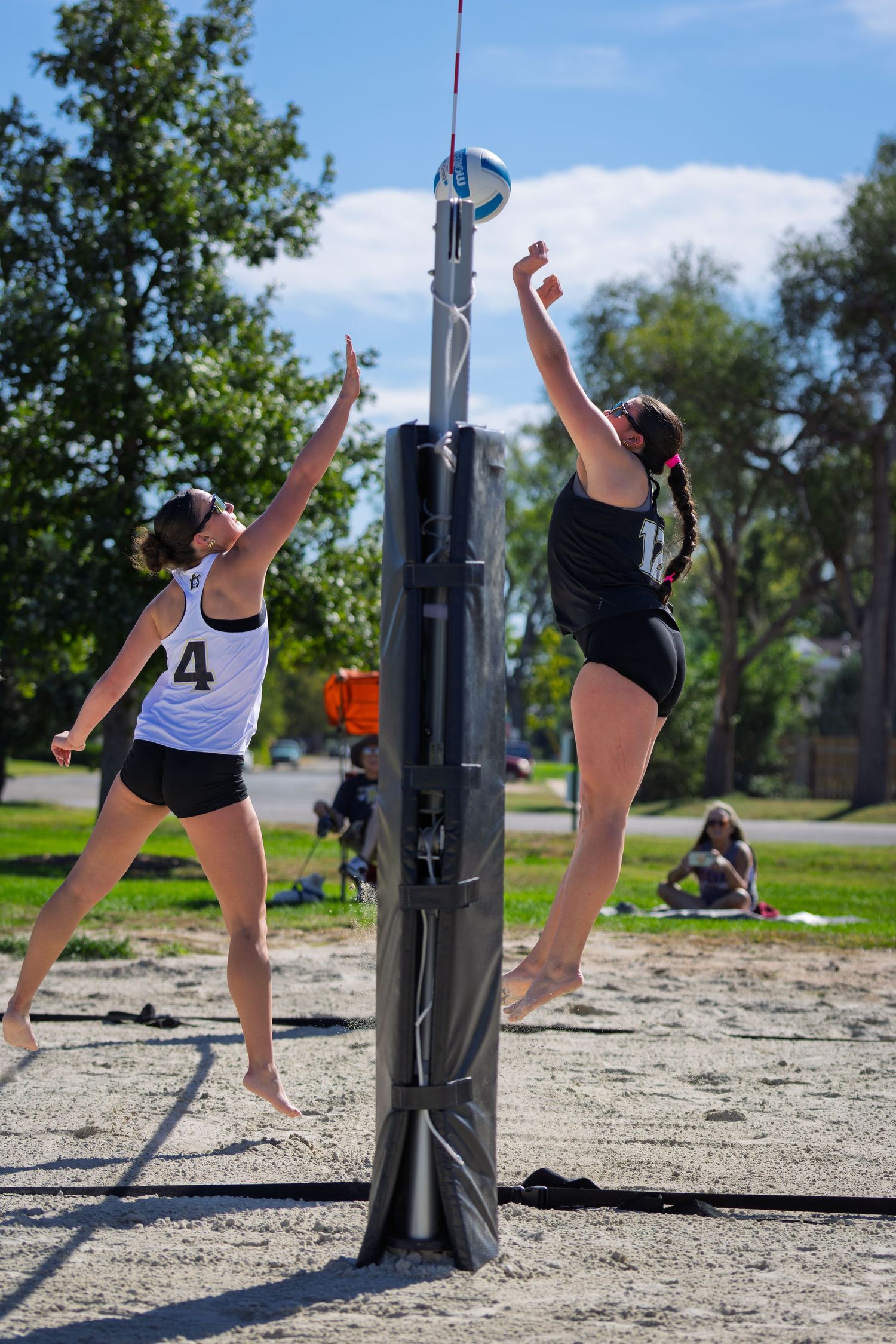 Two female beach volleyball players jump at the net during a competitive outdoor sand court match.
