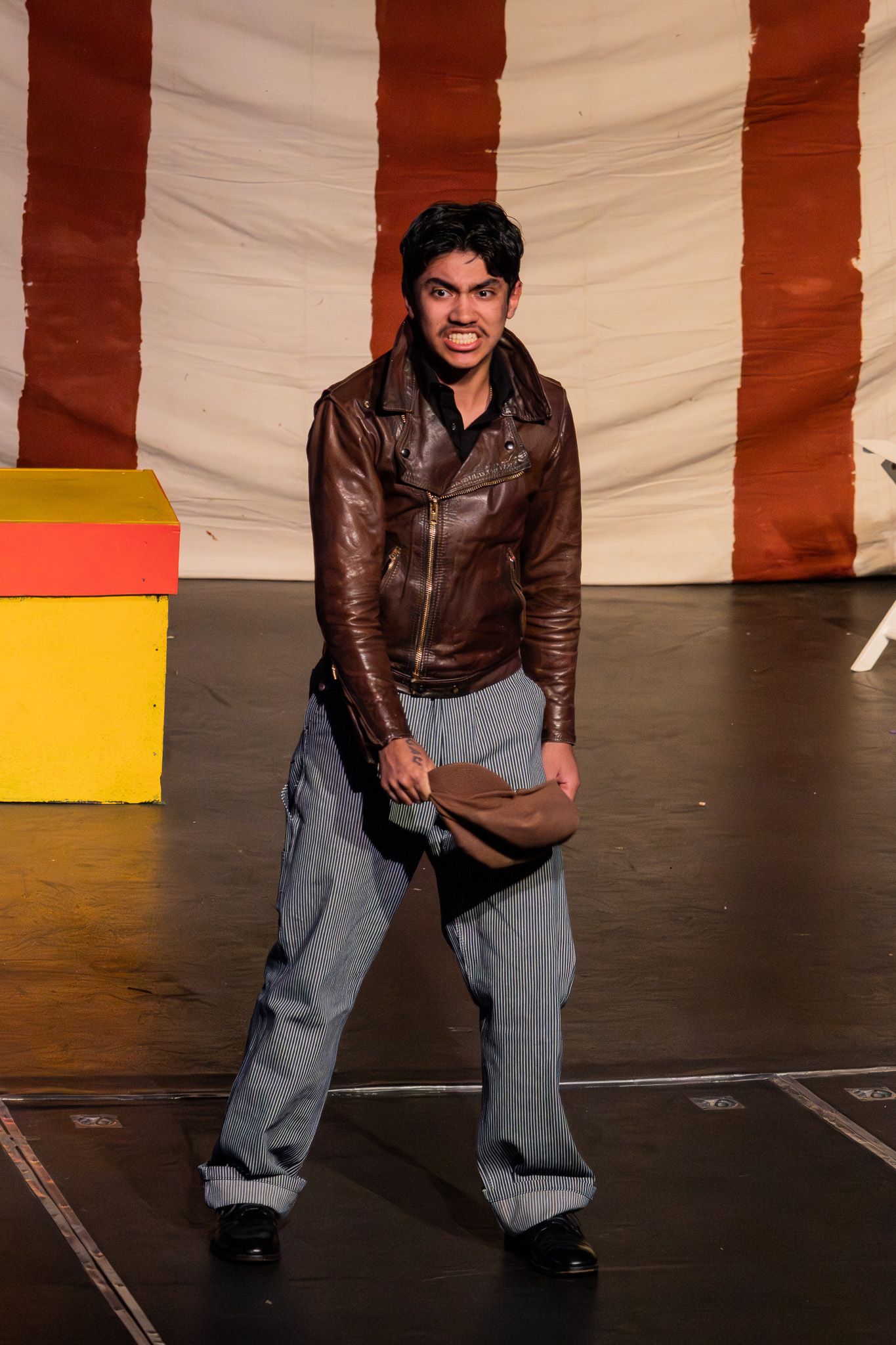 Young male actor performs dramatically on stage wearing a brown leather jacket in a theater production.