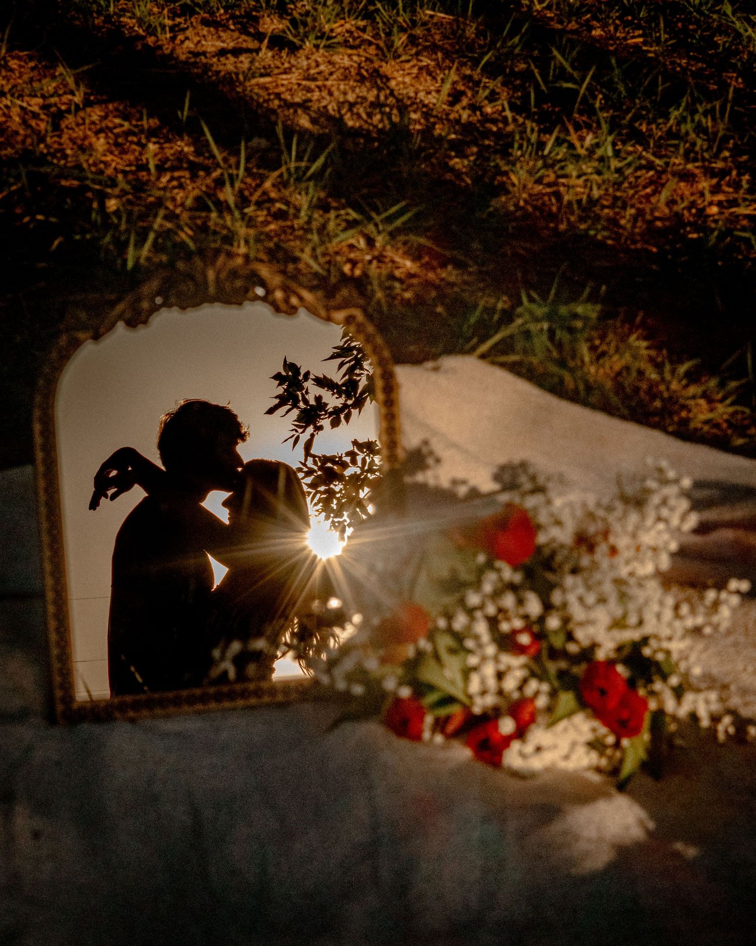 Romantic silhouette reflected in an ornate mirror on a blanket surrounded by red and white flowers.