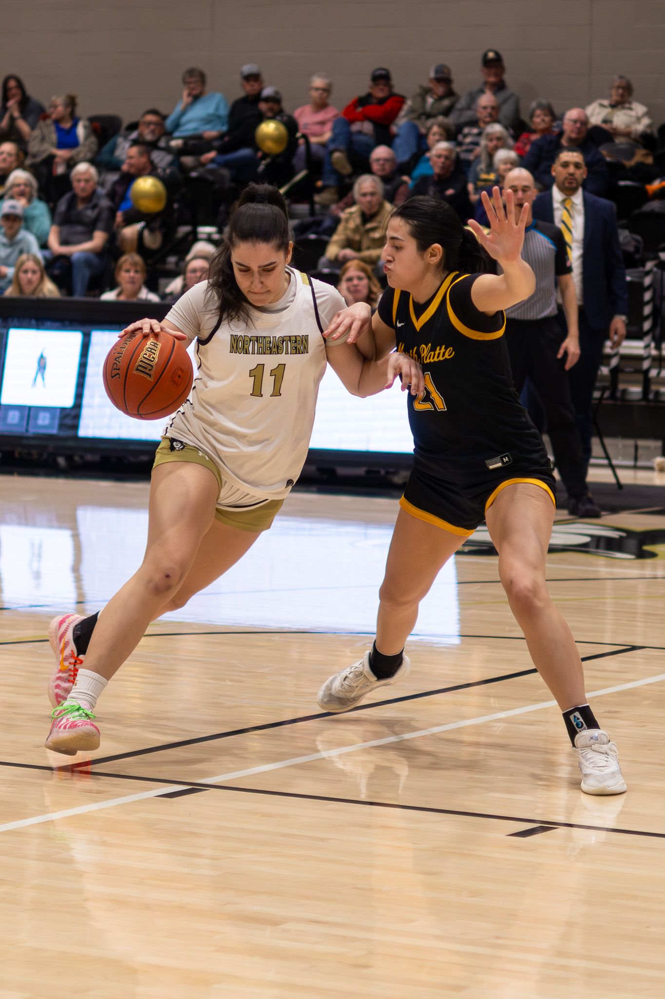 Northeastern female basketball player number 11 drives past a defender in a packed indoor arena.