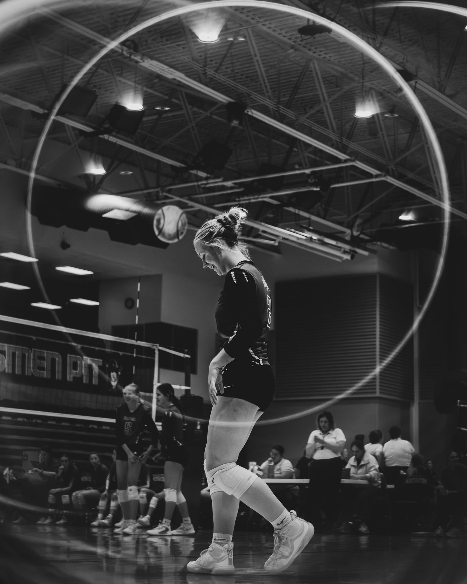 Female volleyball player prepares to serve ball in dramatic circular lens effect black and white photo.