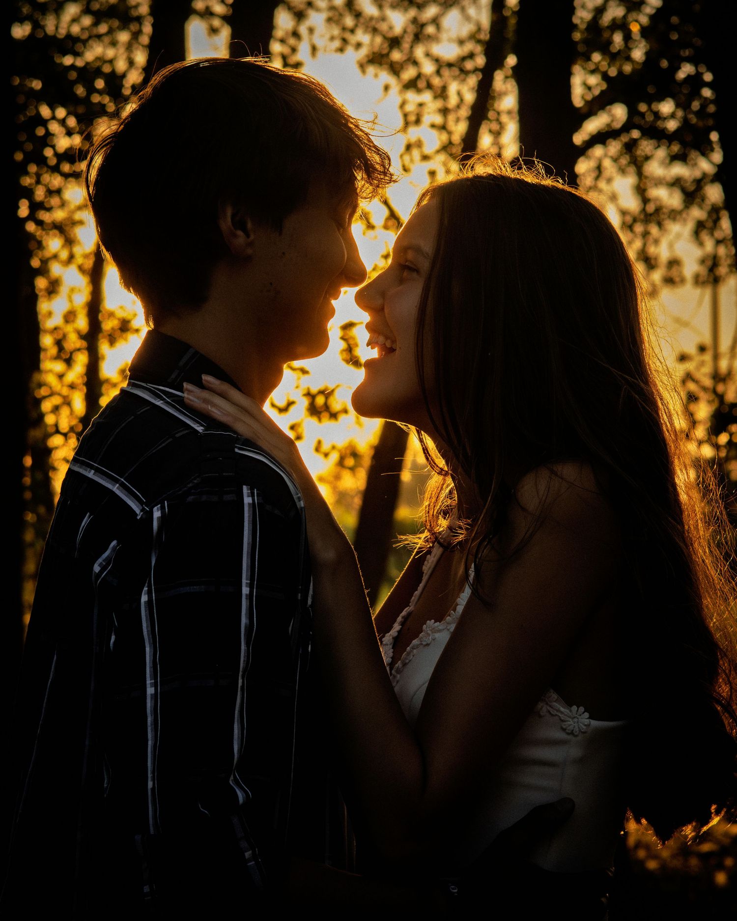 Teen couple sharing a romantic moment face to face in a glowing golden sunset forest.