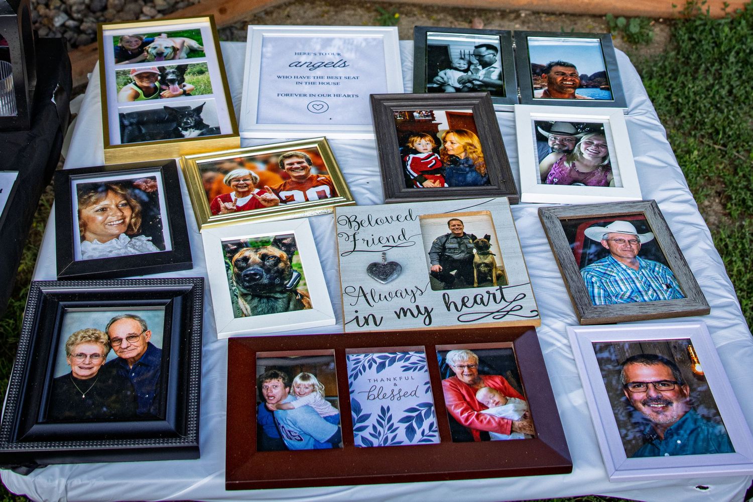 Memorial table display with framed photos, flowers, and heartfelt signs reading Always in My Heart at an outdoor tribute.