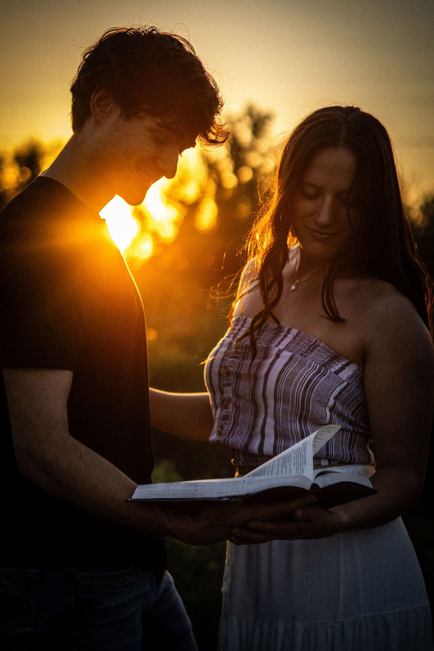Young couple reading a Bible together outdoors during a stunning golden sunset.