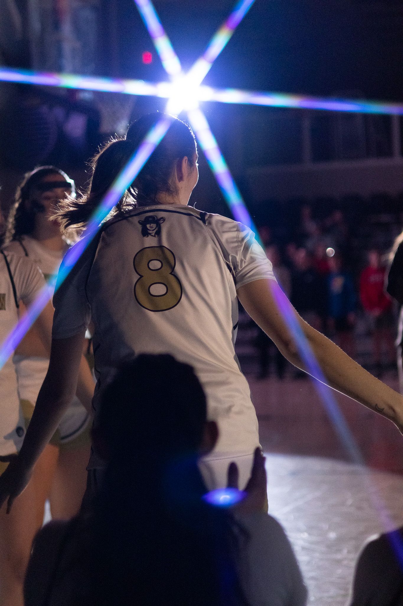 Female basketball player number 8 in white uniform celebrates with teammates under dramatic arena lights.