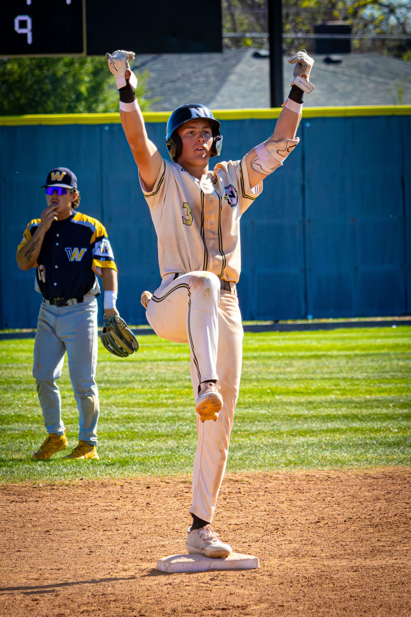A jubilant baseball player raises both arms in celebration while standing on a base.