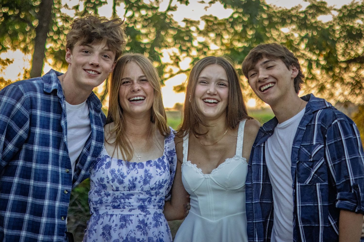 Four smiling teenagers posing together outdoors in casual clothing at golden hour.