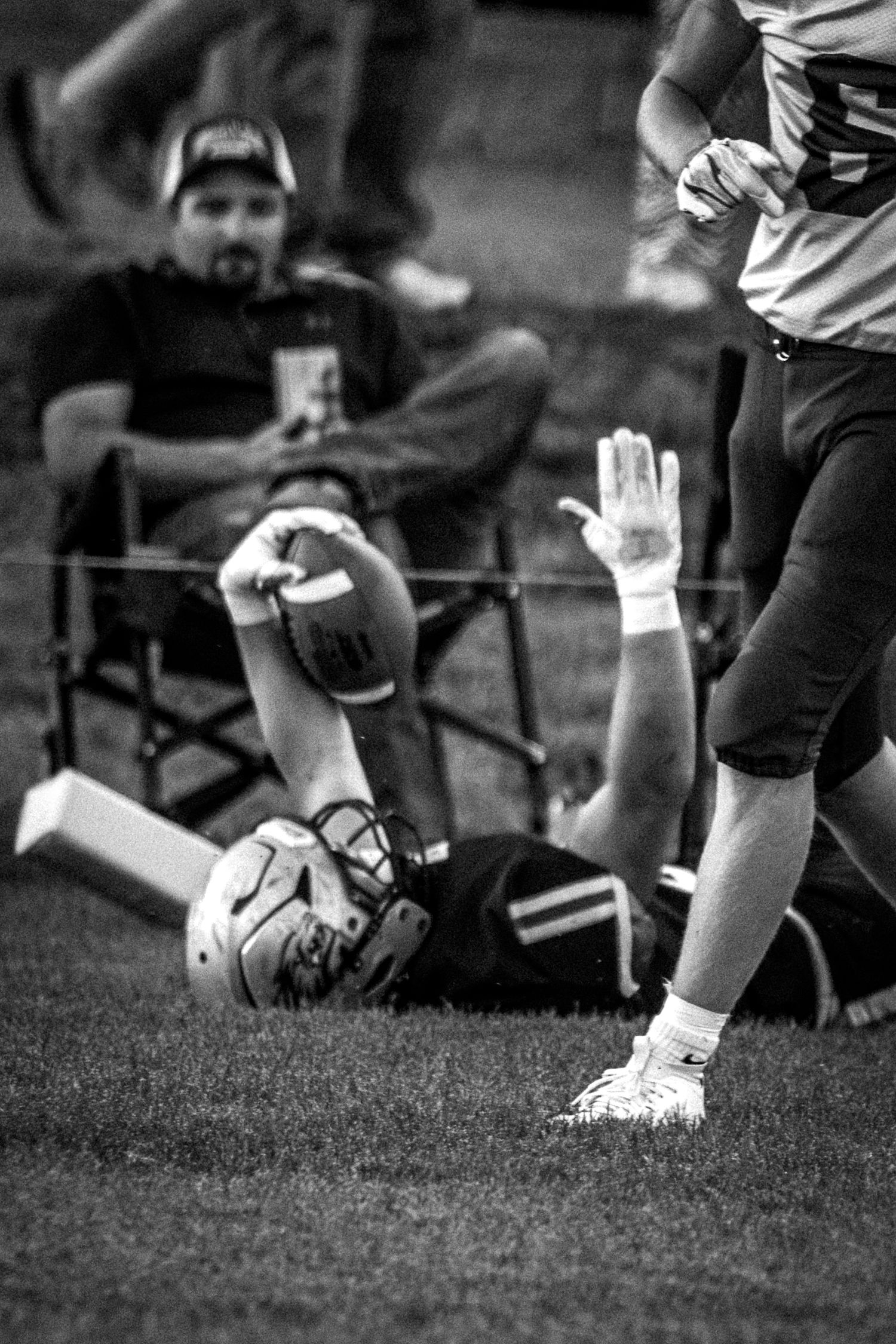 Black and white photo of a football player lying on the ground holding the ball up after a play.