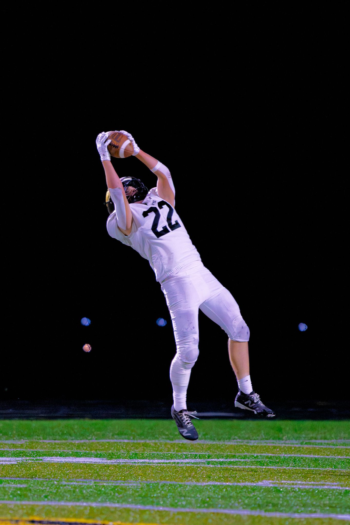 Football player number 22 in white uniform leaps to make a catch during a nighttime football game.
