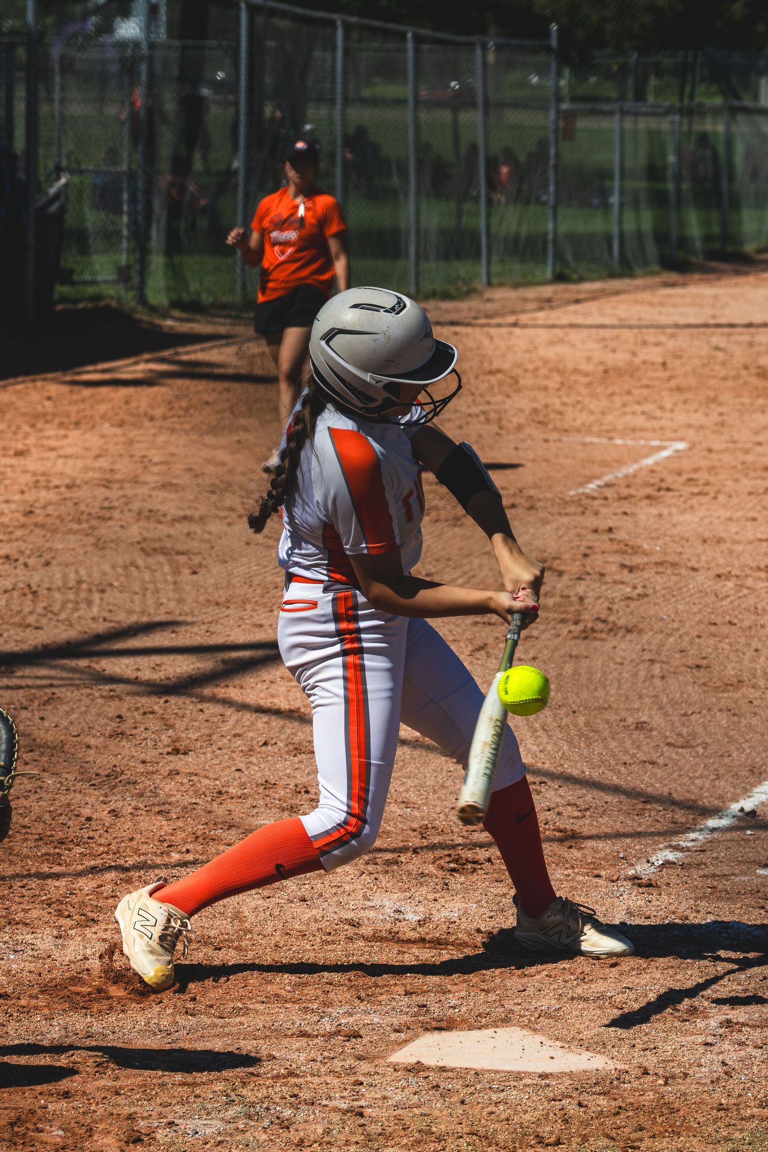 Softball batter in orange and white Tigers uniform making contact with a yellow softball.