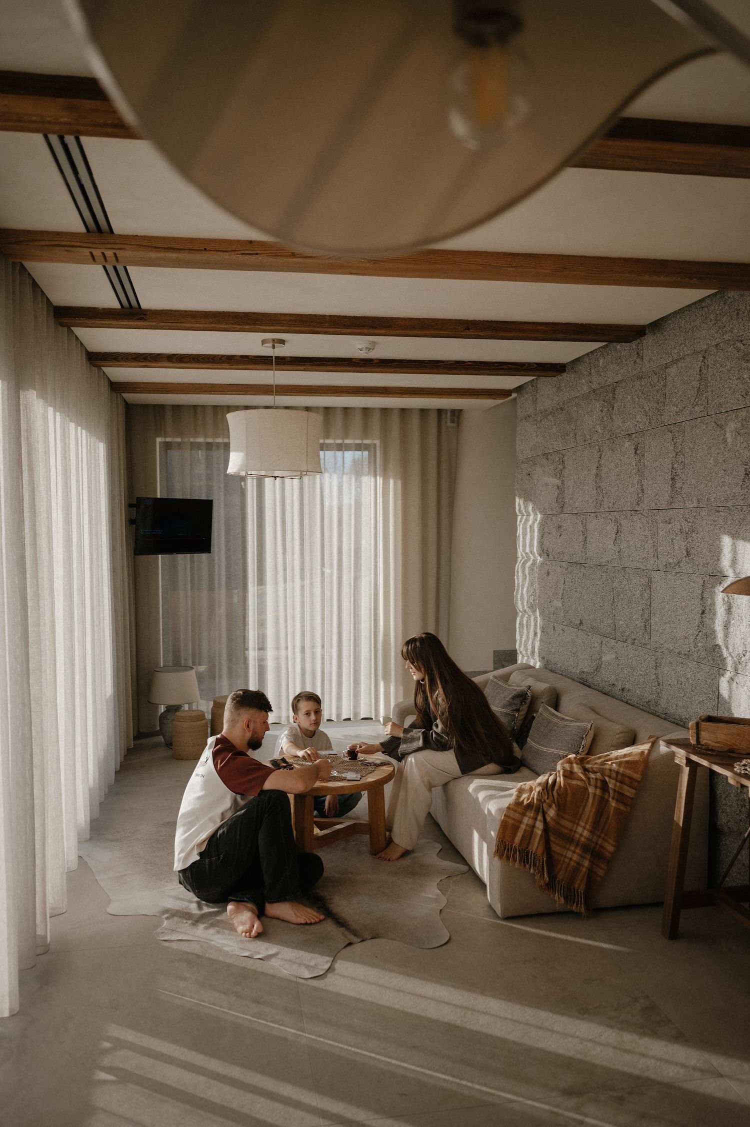 Family of three enjoying quality time together in a modern living room with exposed wooden beams and stone walls.