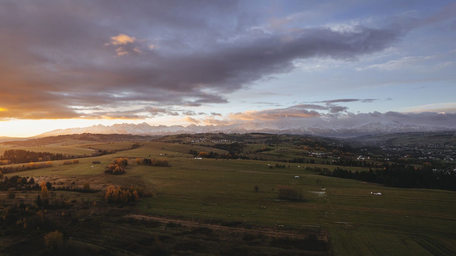 Aerial view of lush green countryside valley at sunset with dramatic cloudy sky and distant mountains.