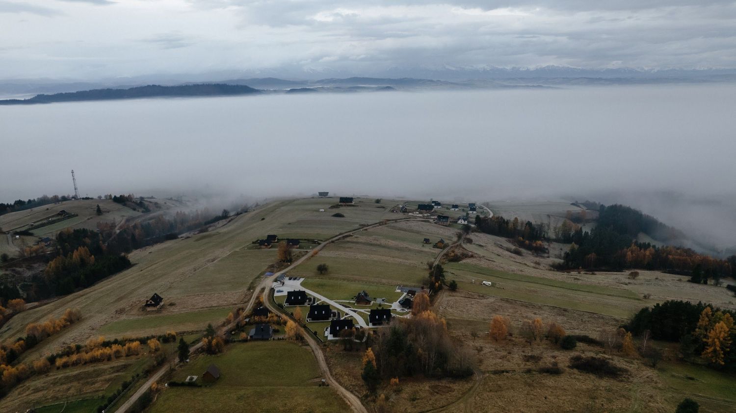 Aerial view of a hilltop farm estate rising above a sea of clouds on an overcast autumn day.