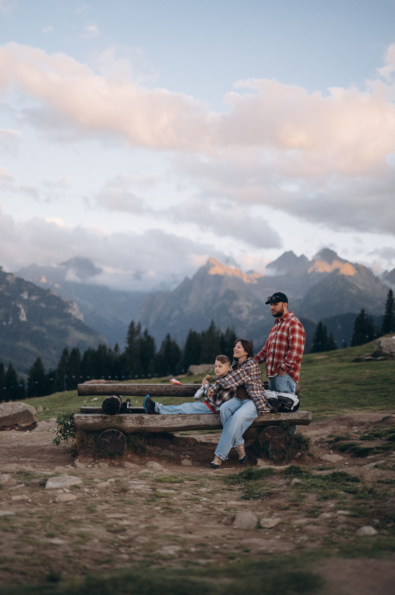 Couple relaxing on a wooden bench with panoramic mountain views at sunset in the Dolomites.